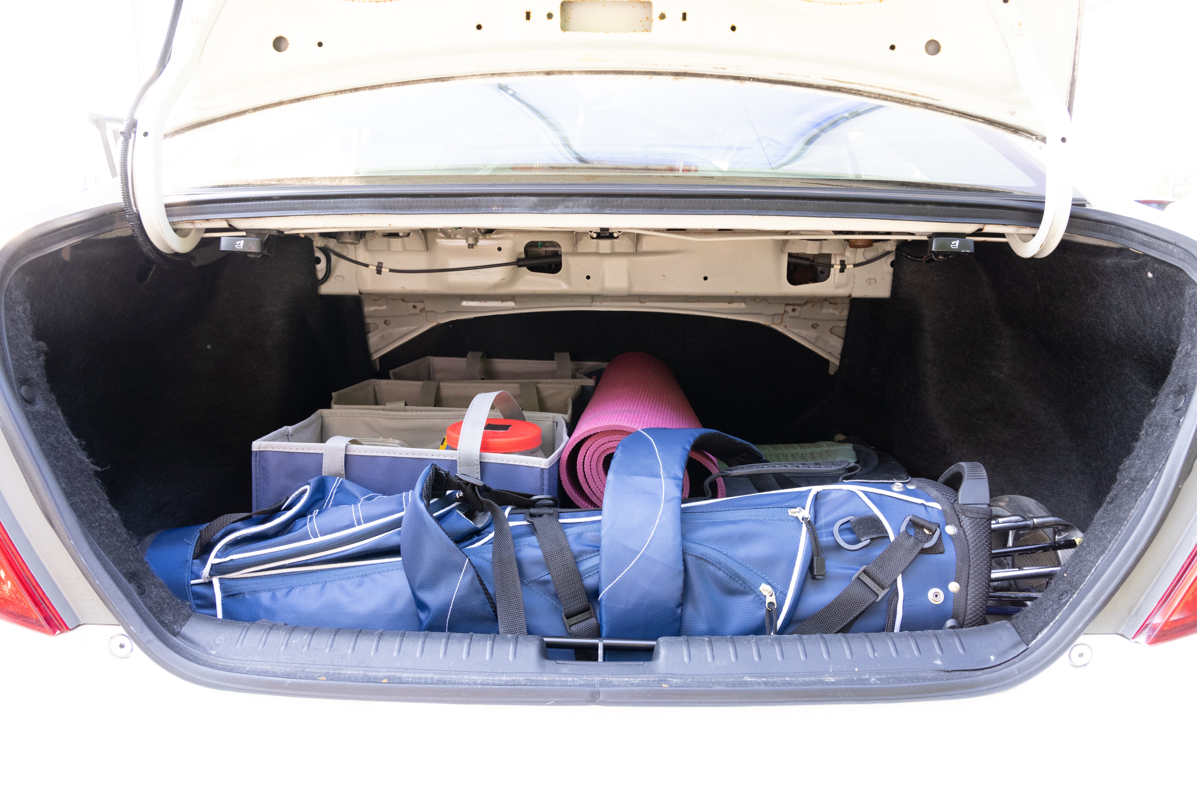 The trunk area is open giving a full view of the trunk area. A baby stroller, four grocery carriers, a yoga mat, and a set of golf clubs are placed inside.