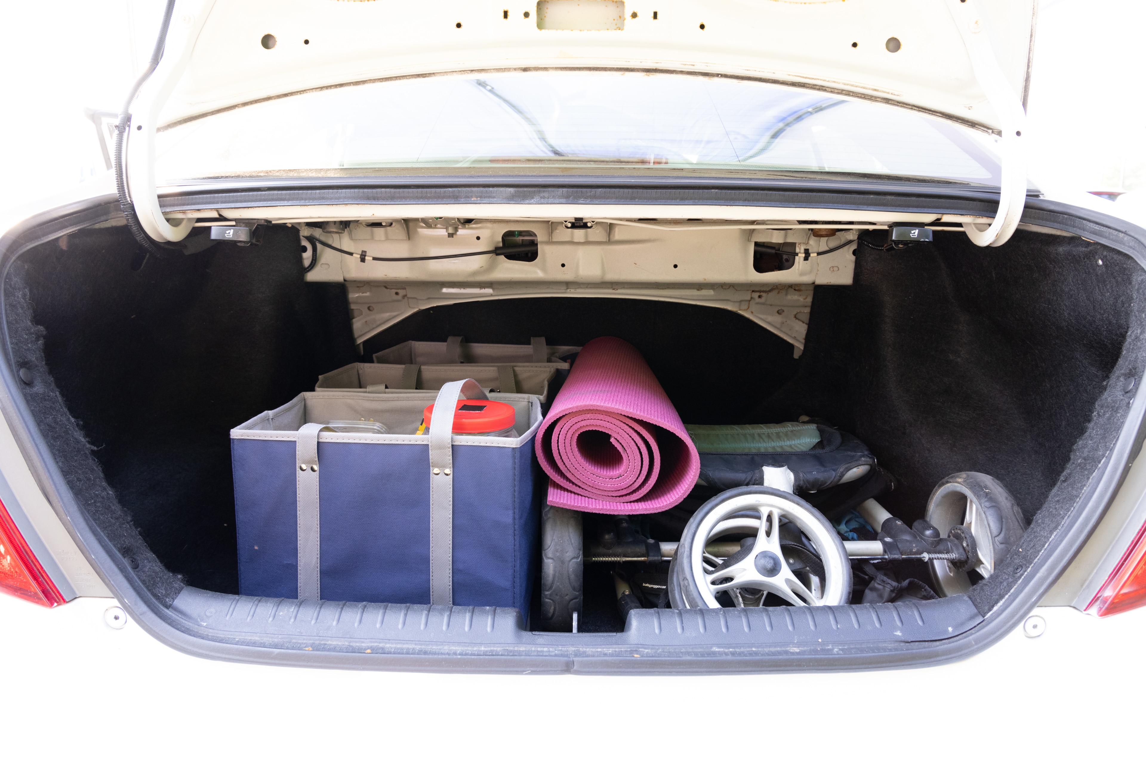The trunk area is open giving a full view of the trunk area. A baby stroller, four grocery carriers, a yoga mat, and a set of golf clubs are placed inside.