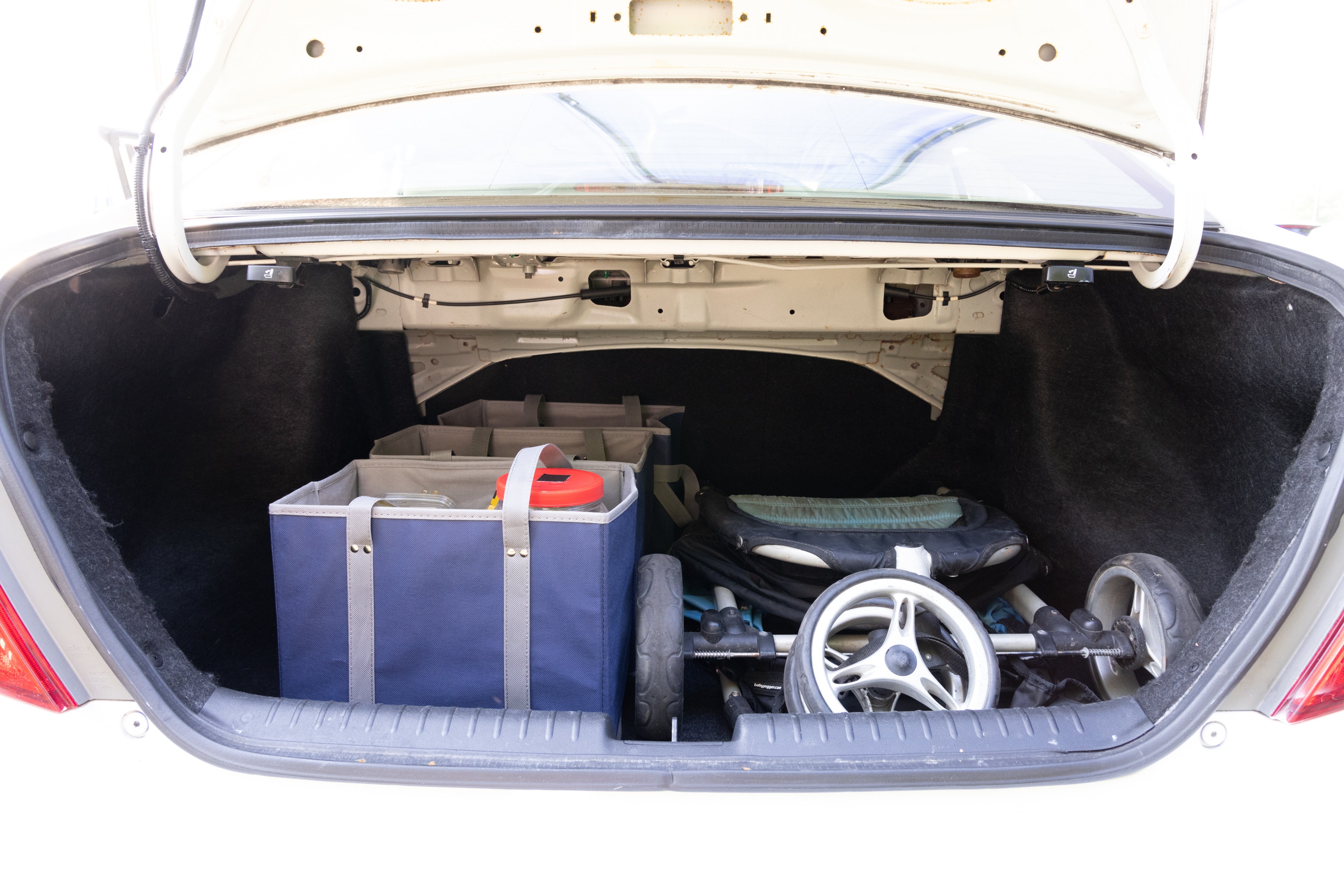 The trunk area is open giving a full view of the trunk area. A baby stroller, four grocery carriers, a yoga mat, and a set of golf clubs are placed inside.