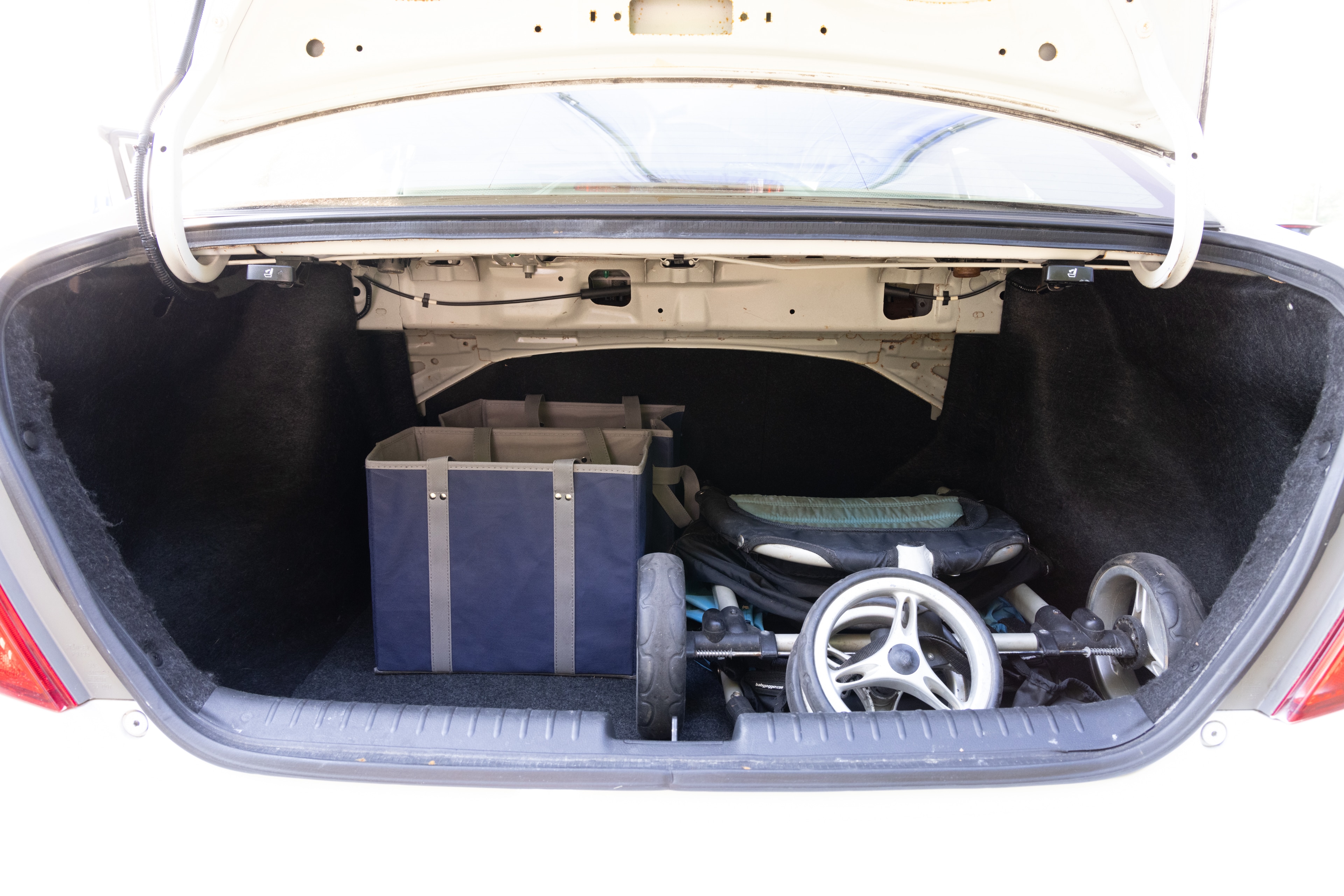 The trunk area is open giving a full view of the trunk area. A baby stroller, four grocery carriers, a yoga mat, and a set of golf clubs are placed inside.