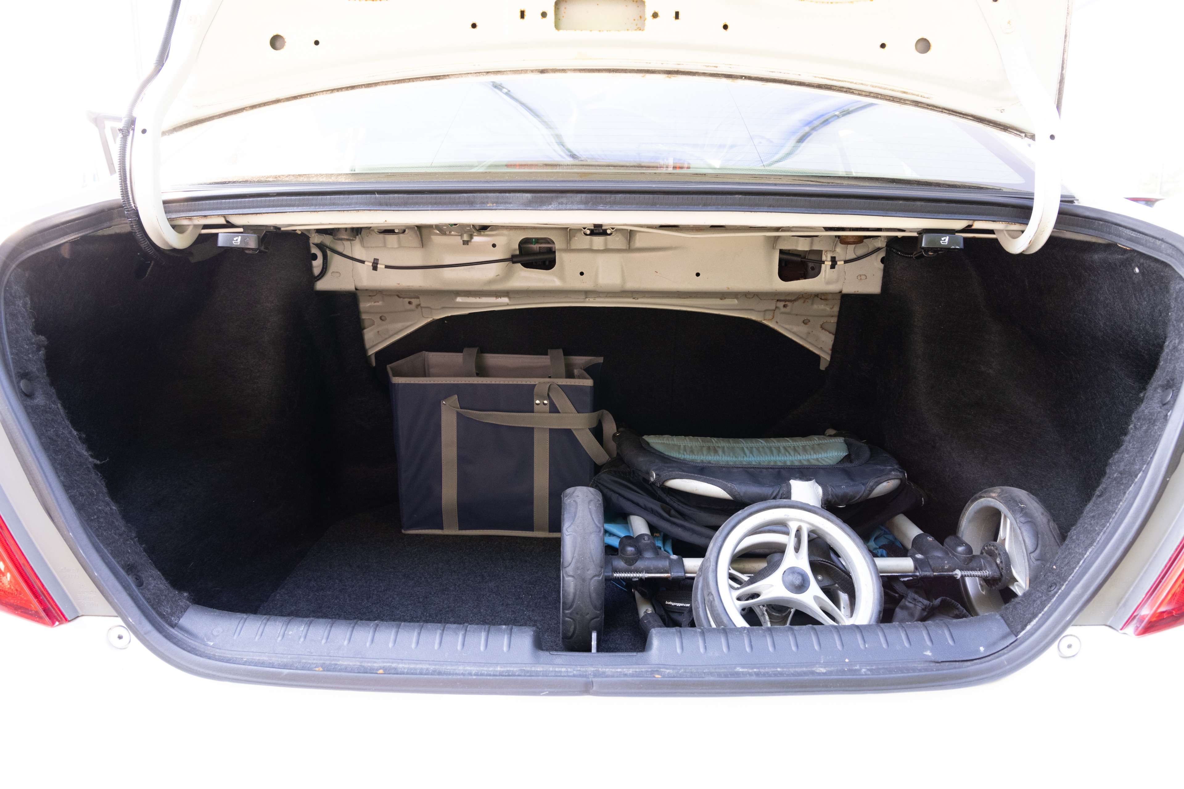 The trunk area is open giving a full view of the trunk area. A baby stroller, four grocery carriers, a yoga mat, and a set of golf clubs are placed inside.