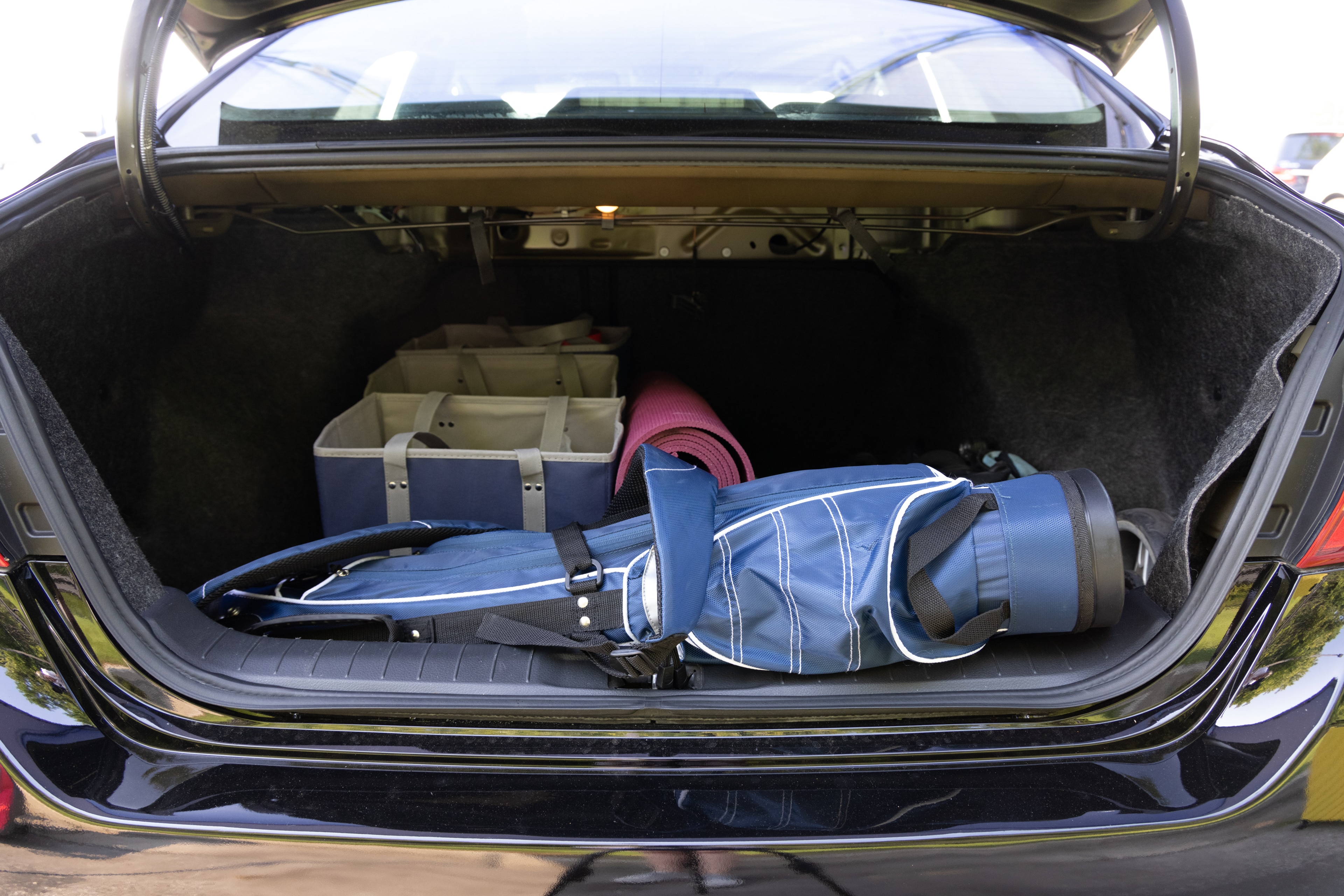The trunk area is open giving a full view of the trunk area. A baby stroller, four grocery carriers, a yoga mat, and a set of golf clubs are placed inside.