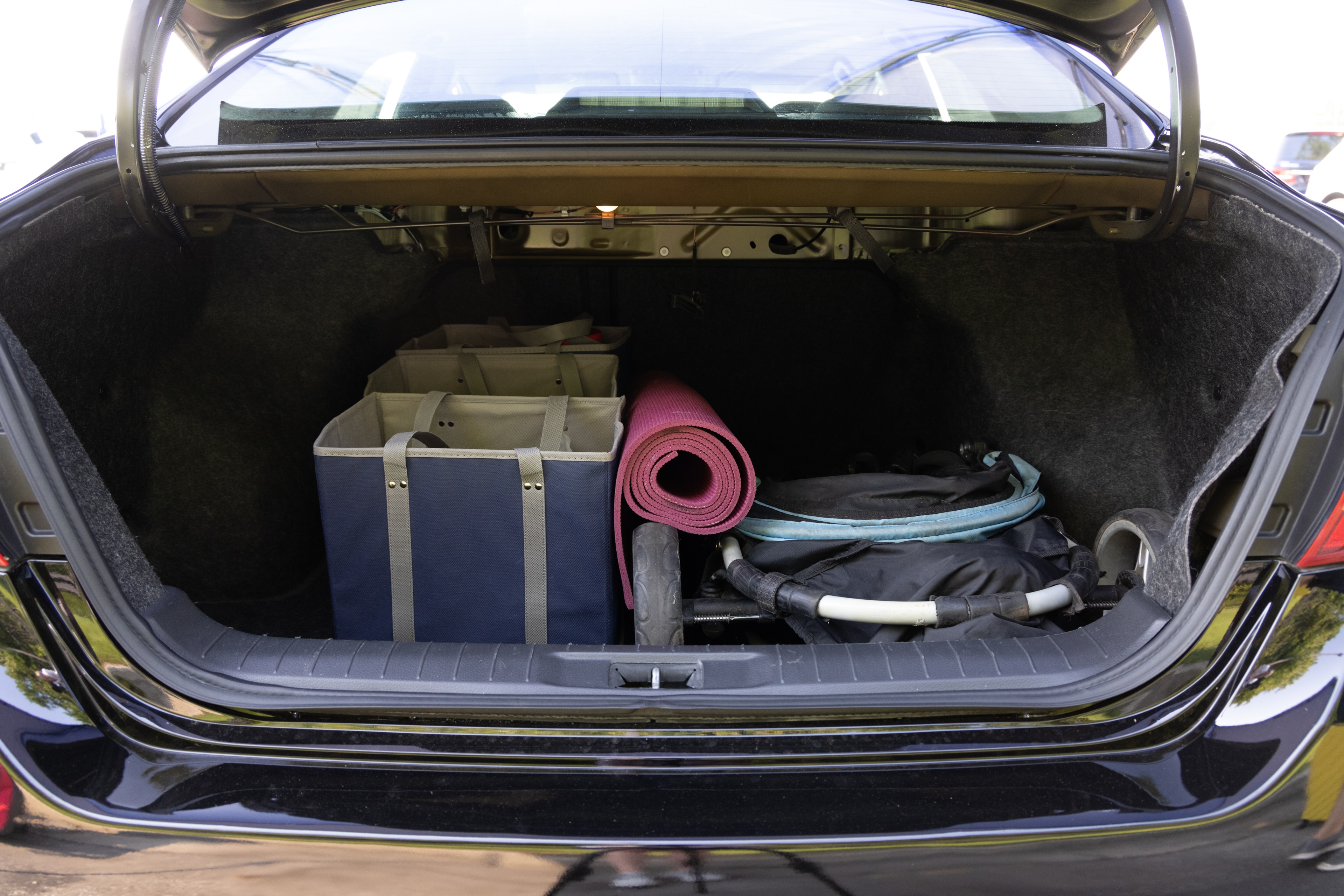 The trunk area is open giving a full view of the trunk area. A baby stroller, four grocery carriers, a yoga mat, and a set of golf clubs are placed inside.