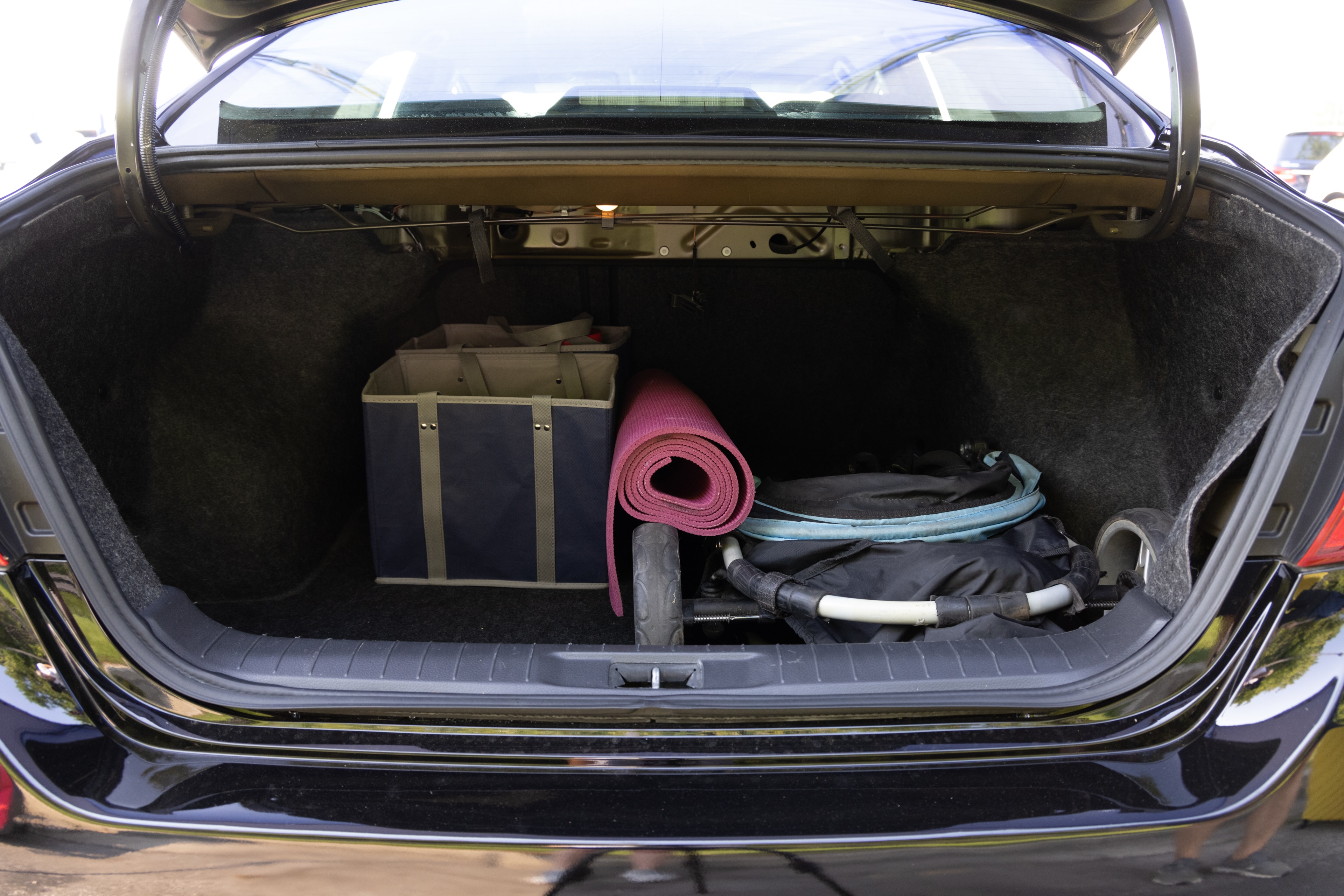 The trunk area is open giving a full view of the trunk area. A baby stroller, four grocery carriers, a yoga mat, and a set of golf clubs are placed inside.