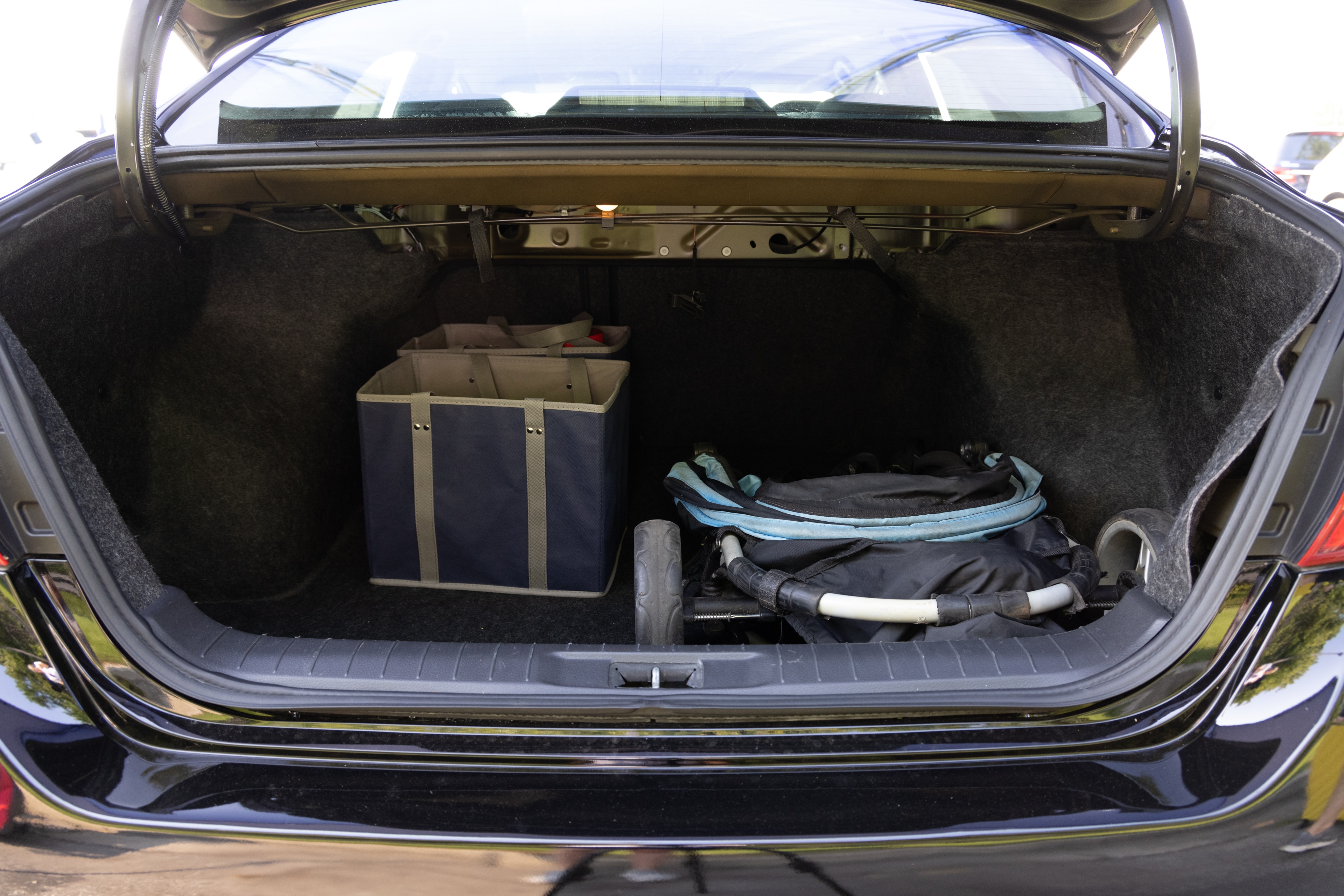 The trunk area is open giving a full view of the trunk area. A baby stroller, four grocery carriers, a yoga mat, and a set of golf clubs are placed inside.