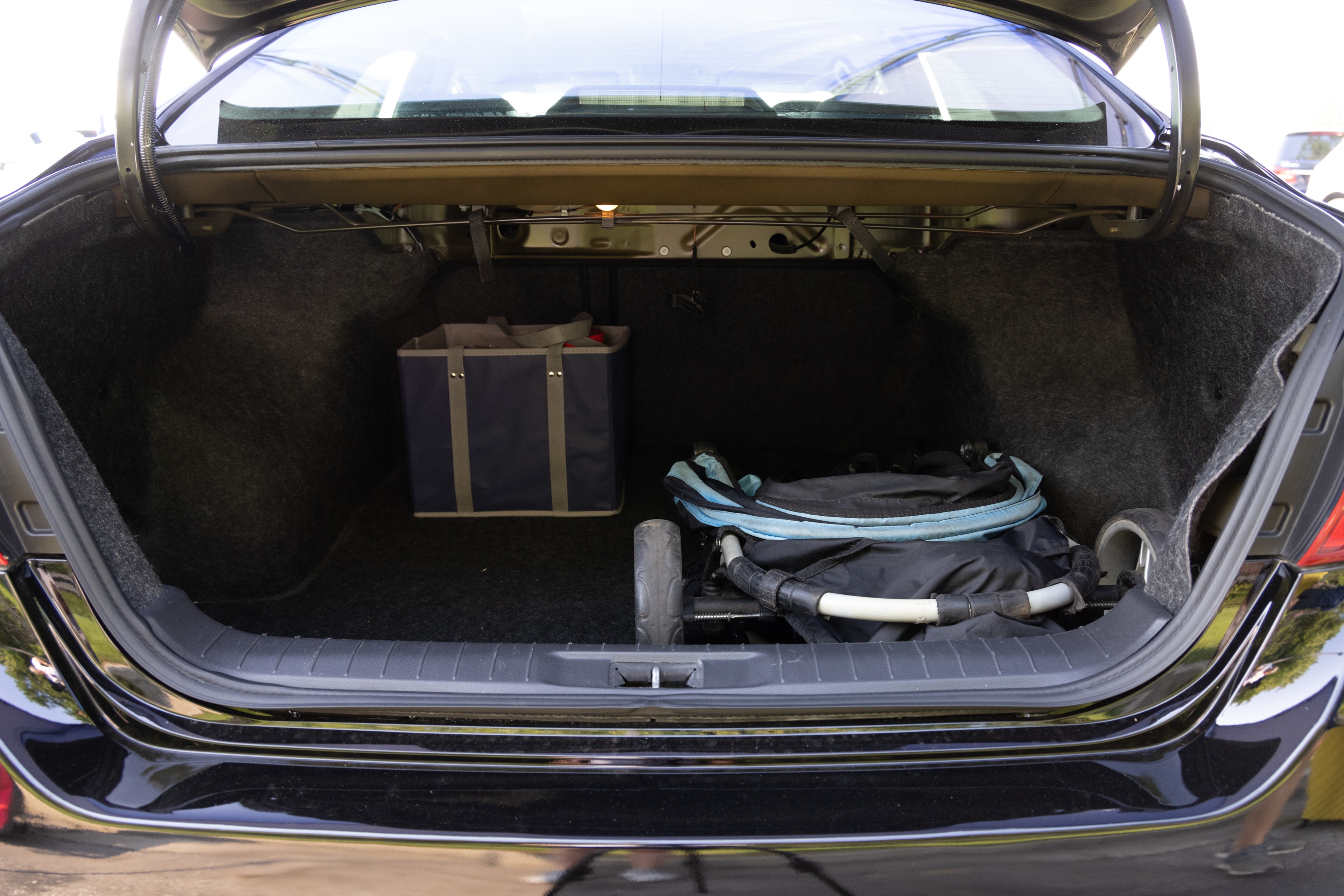 The trunk area is open giving a full view of the trunk area. A baby stroller, four grocery carriers, a yoga mat, and a set of golf clubs are placed inside.