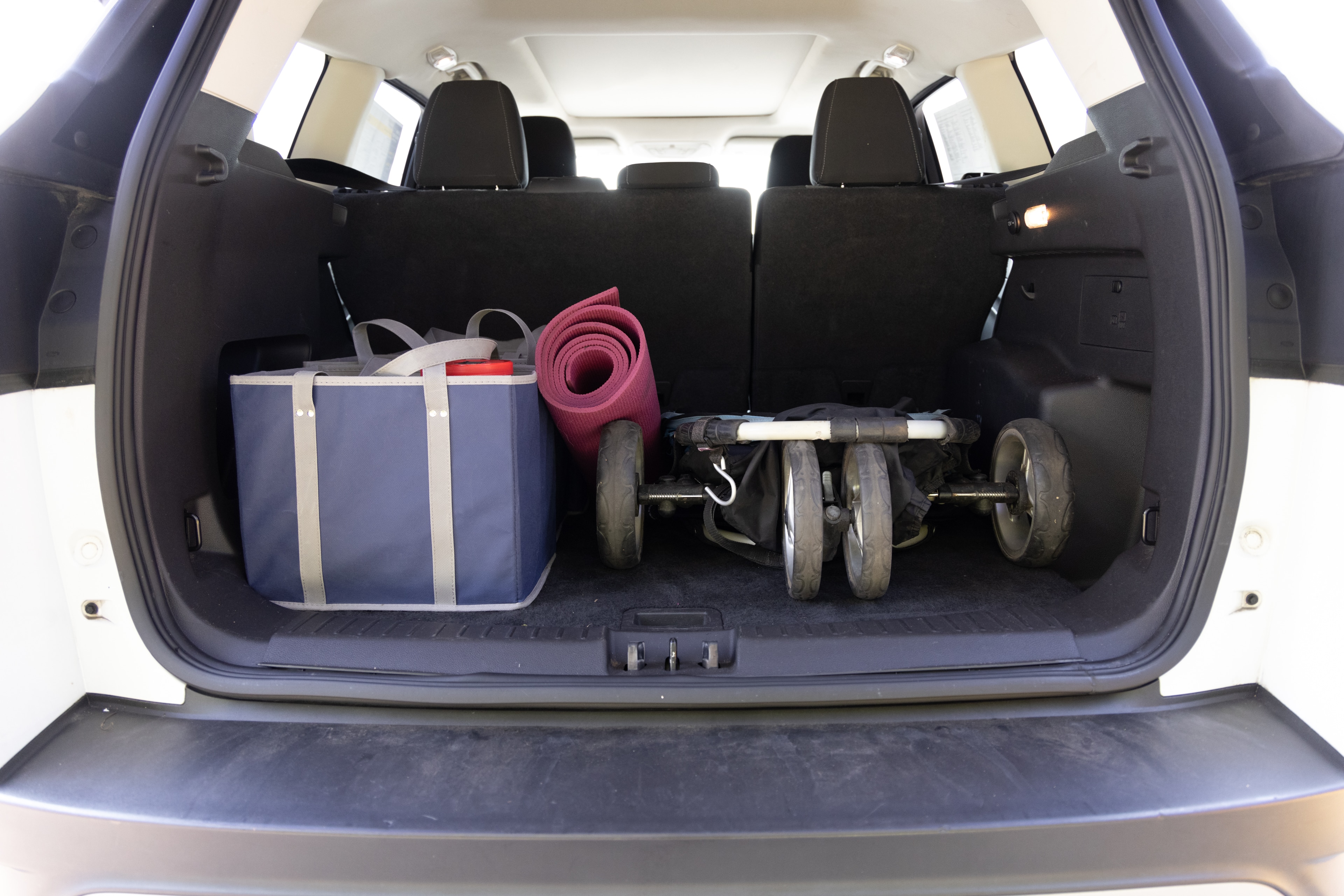 The cargo area is open giving a full view of the trunk area. A baby stroller, four grocery carriers, a yoga mat, and a set of golf clubs are placed inside.