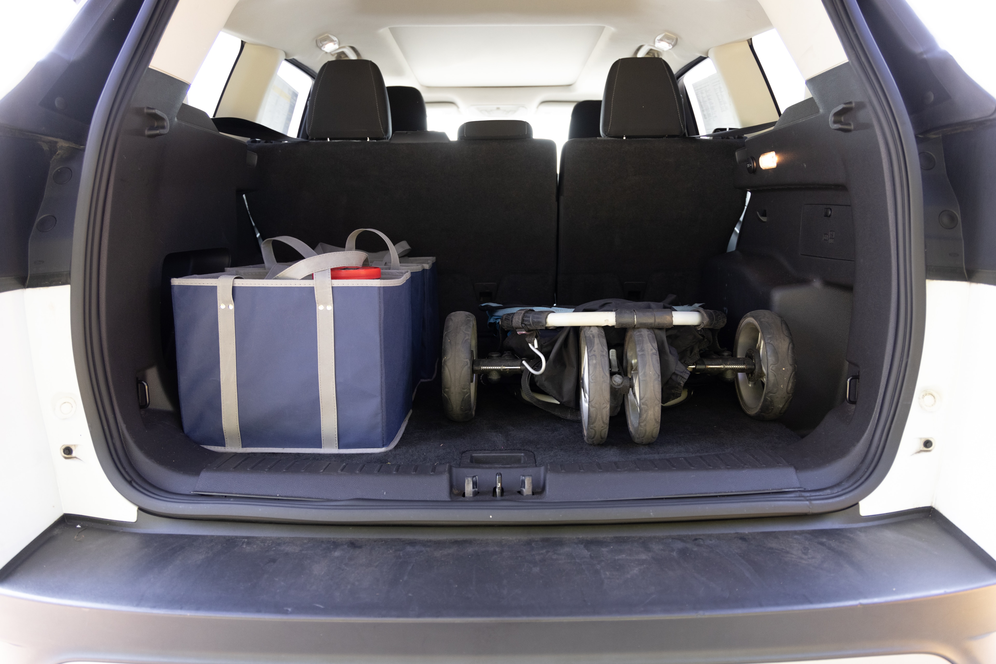 The cargo area is open giving a full view of the trunk area. A baby stroller, four grocery carriers, a yoga mat, and a set of golf clubs are placed inside.