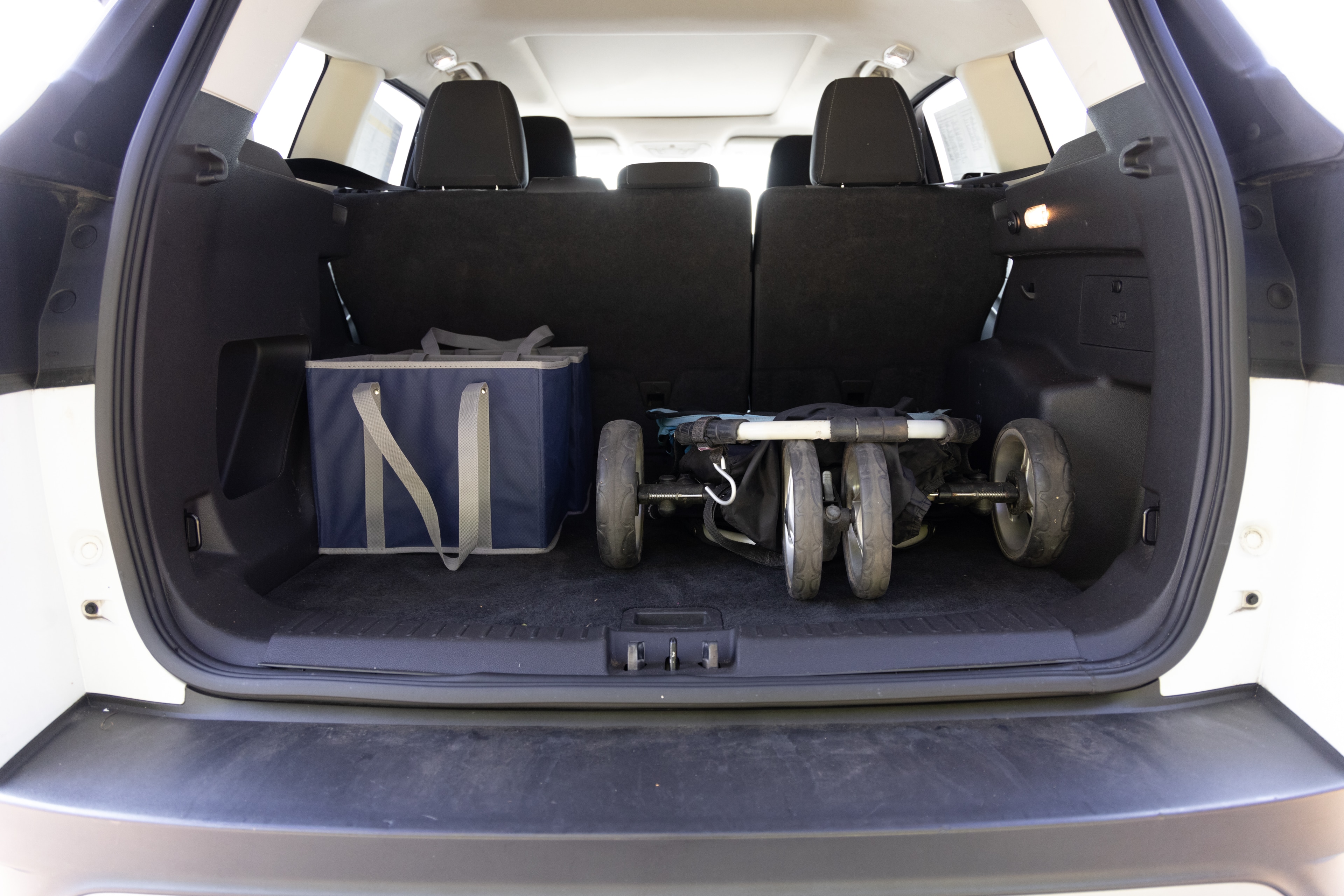 The cargo area is open giving a full view of the trunk area. A baby stroller, four grocery carriers, a yoga mat, and a set of golf clubs are placed inside.
