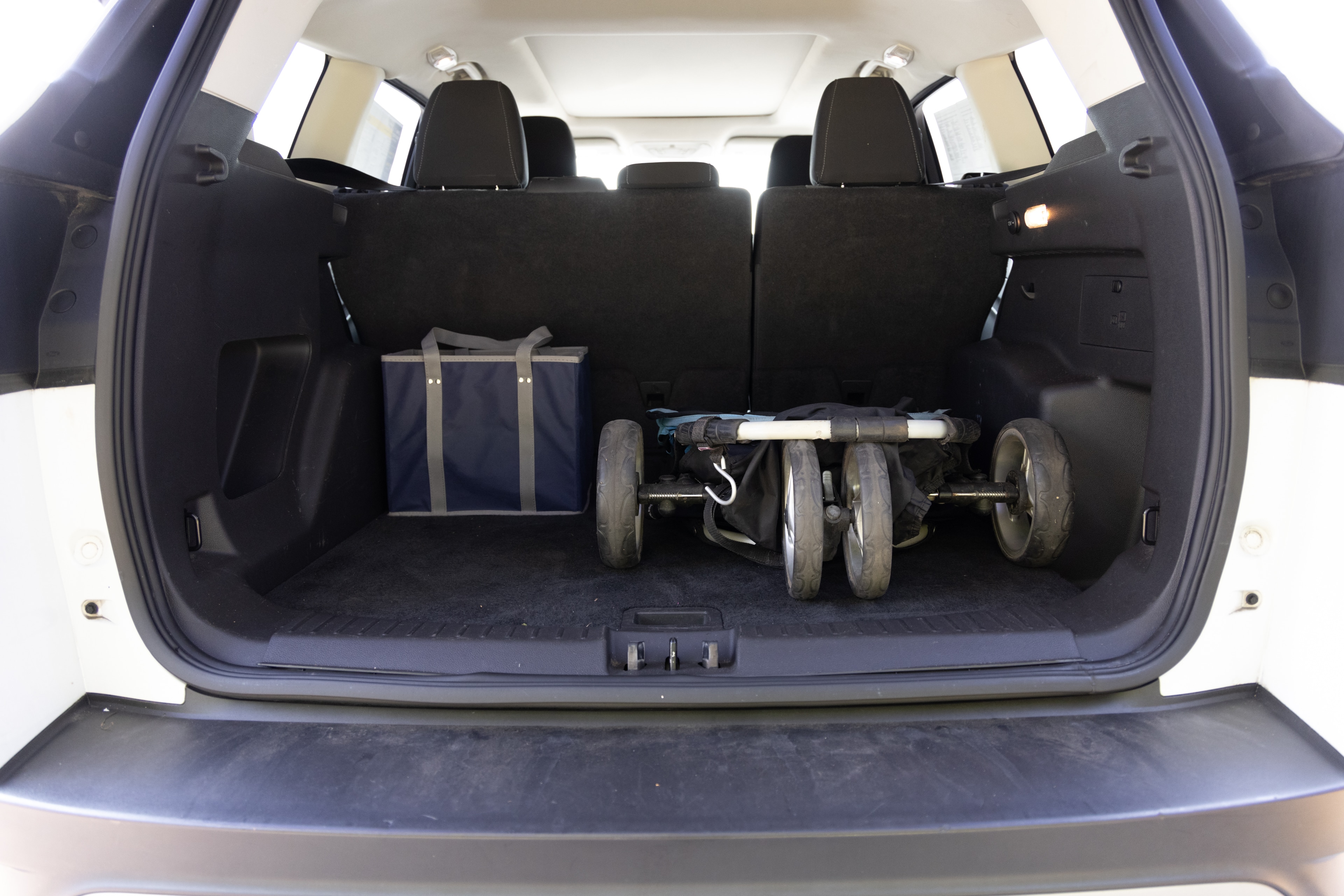 The cargo area is open giving a full view of the trunk area. A baby stroller, four grocery carriers, a yoga mat, and a set of golf clubs are placed inside.