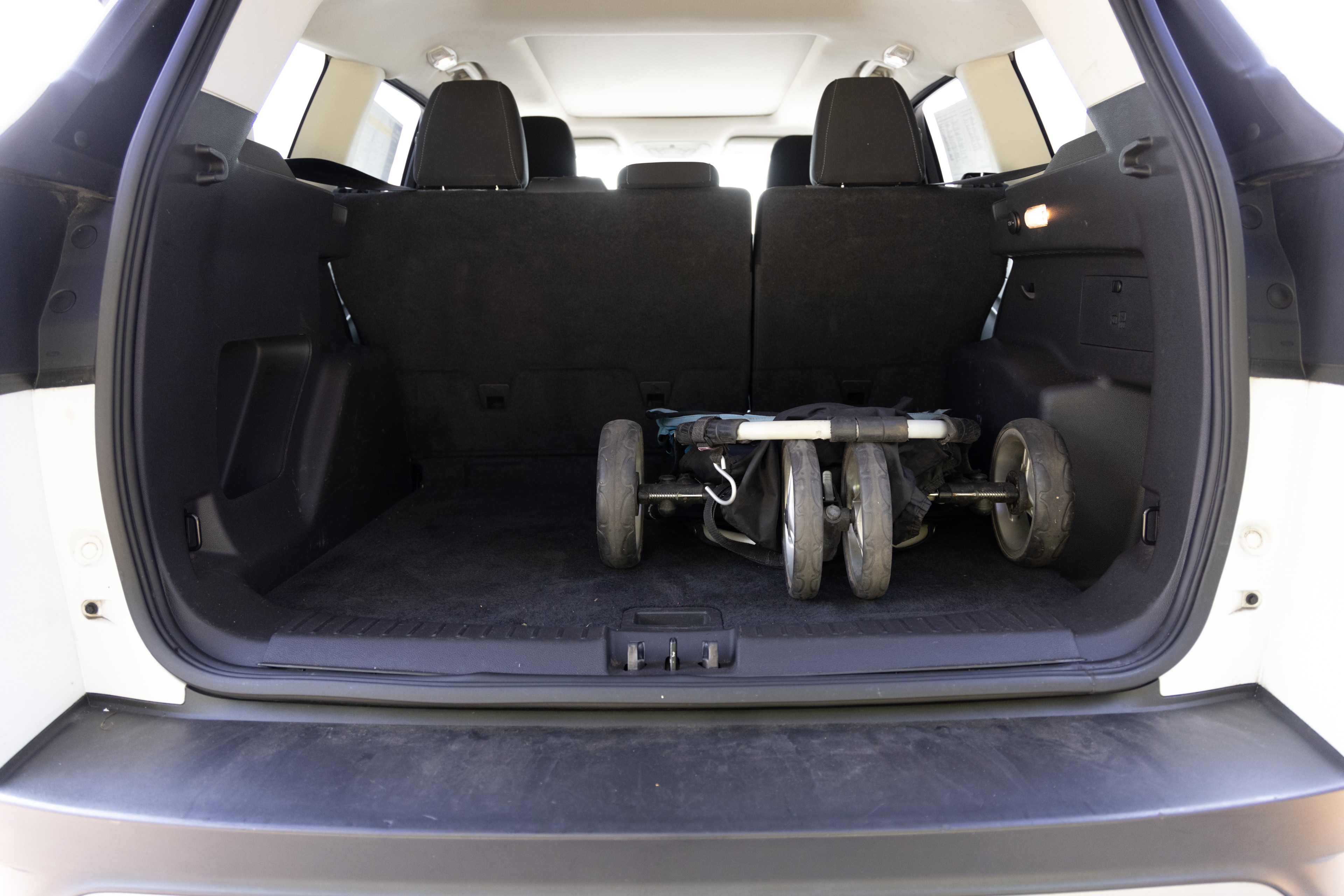 The cargo area is open giving a full view of the trunk area. A baby stroller, four grocery carriers, a yoga mat, and a set of golf clubs are placed inside.