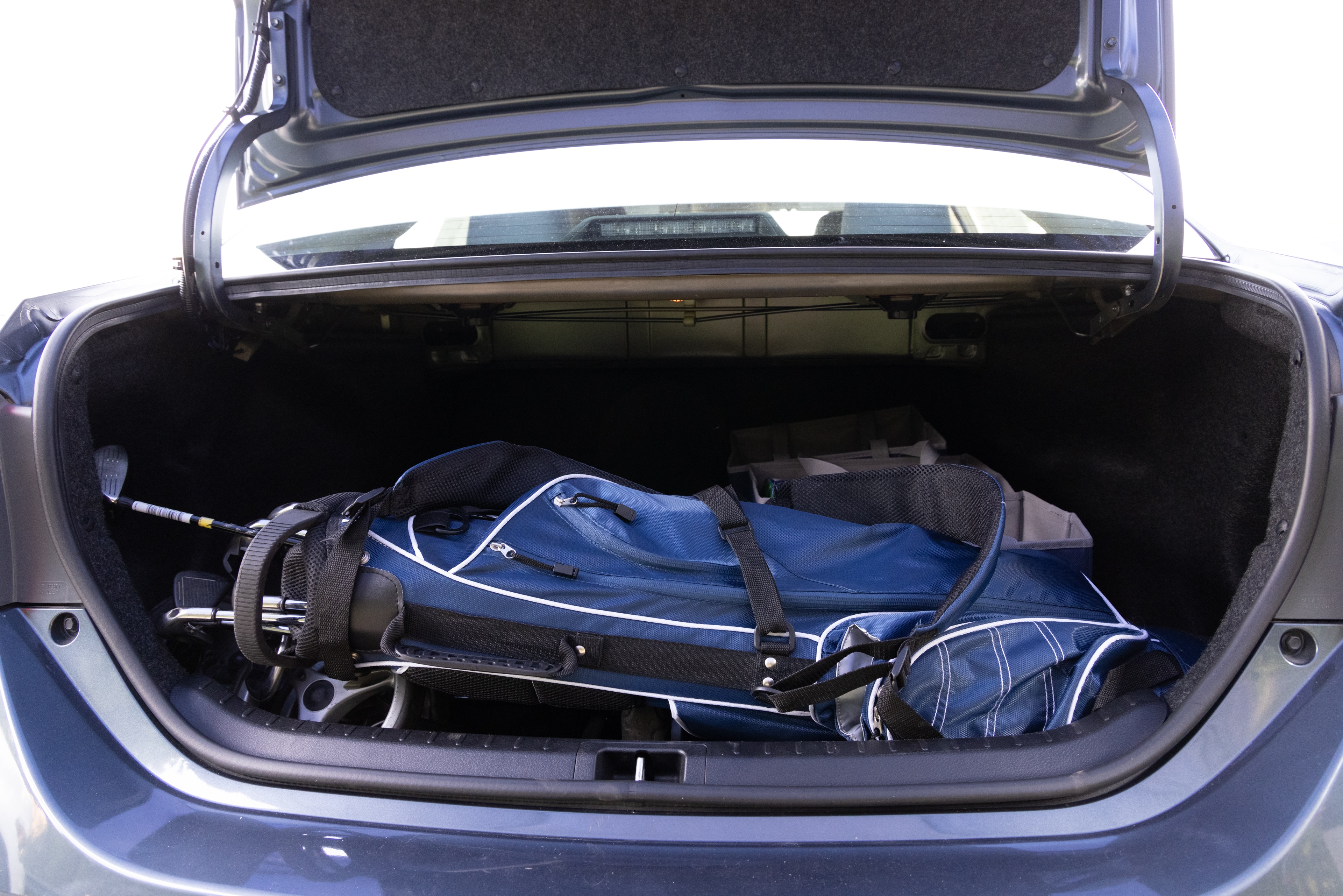 The trunk area is open giving a full view of the trunk area. A baby stroller, four grocery carriers, a yoga mat, and a set of golf clubs are placed inside.