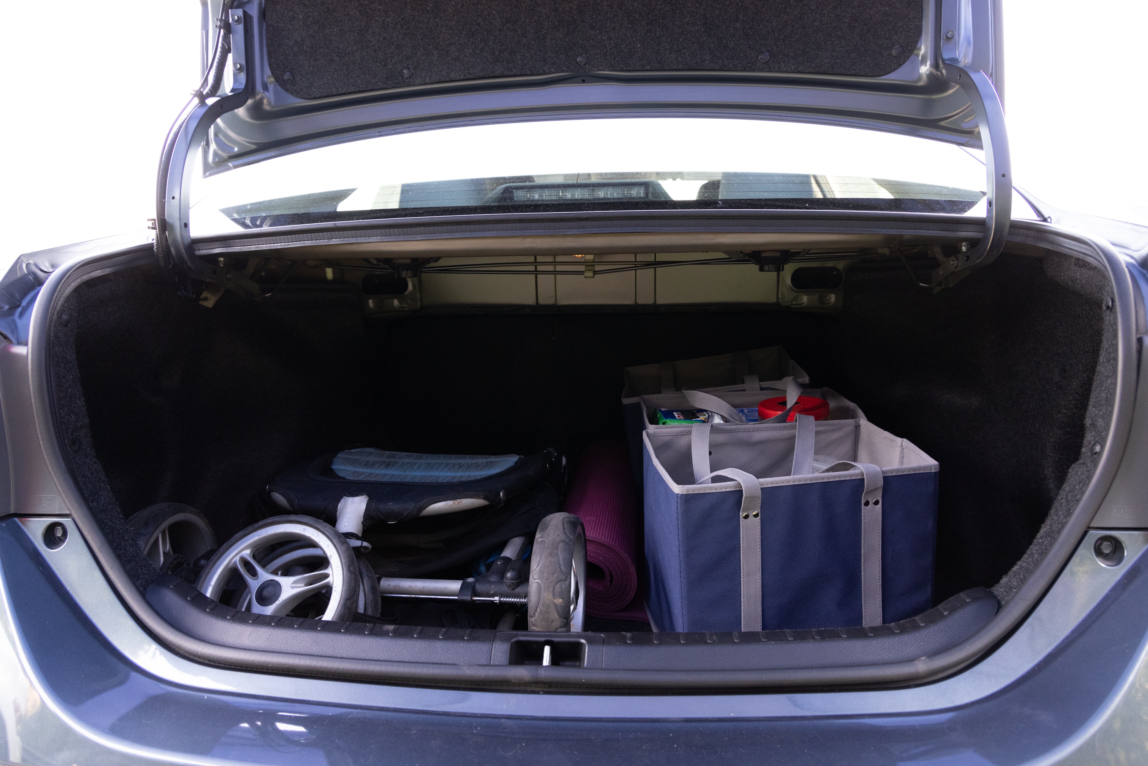 The trunk area is open giving a full view of the trunk area. A baby stroller, four grocery carriers, a yoga mat, and a set of golf clubs are placed inside.