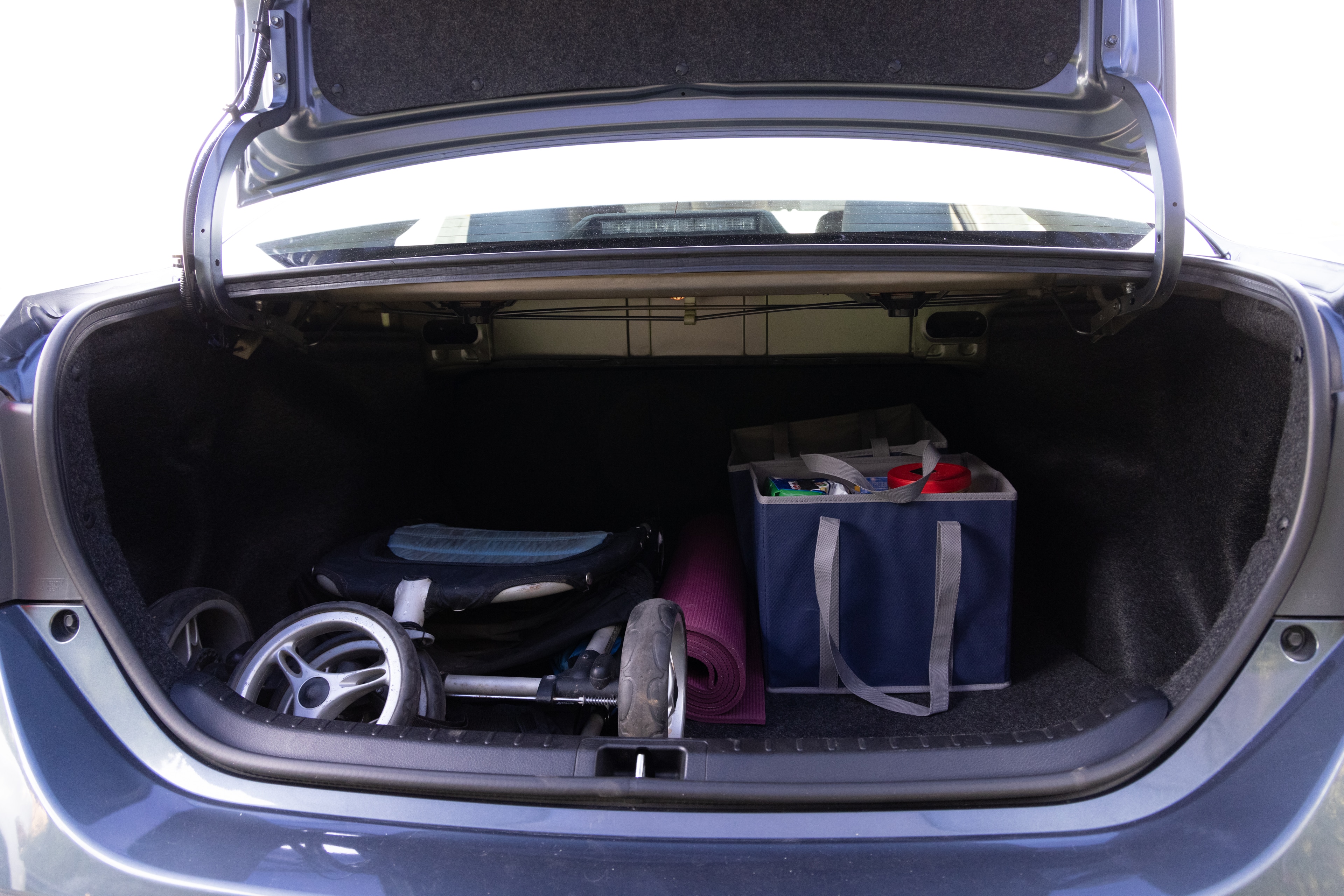 The trunk area is open giving a full view of the trunk area. A baby stroller, four grocery carriers, a yoga mat, and a set of golf clubs are placed inside.