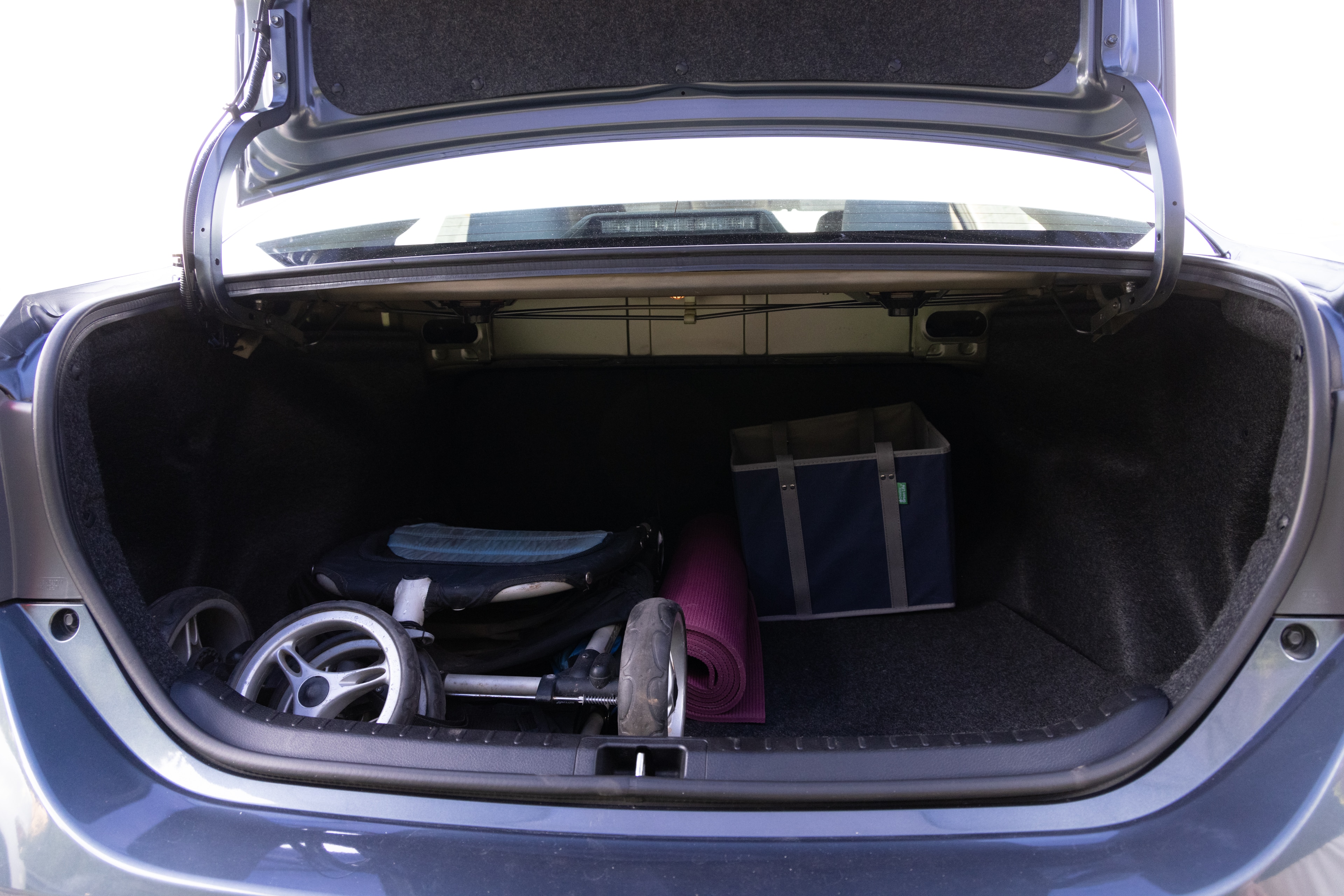 The trunk area is open giving a full view of the trunk area. A baby stroller, four grocery carriers, a yoga mat, and a set of golf clubs are placed inside.