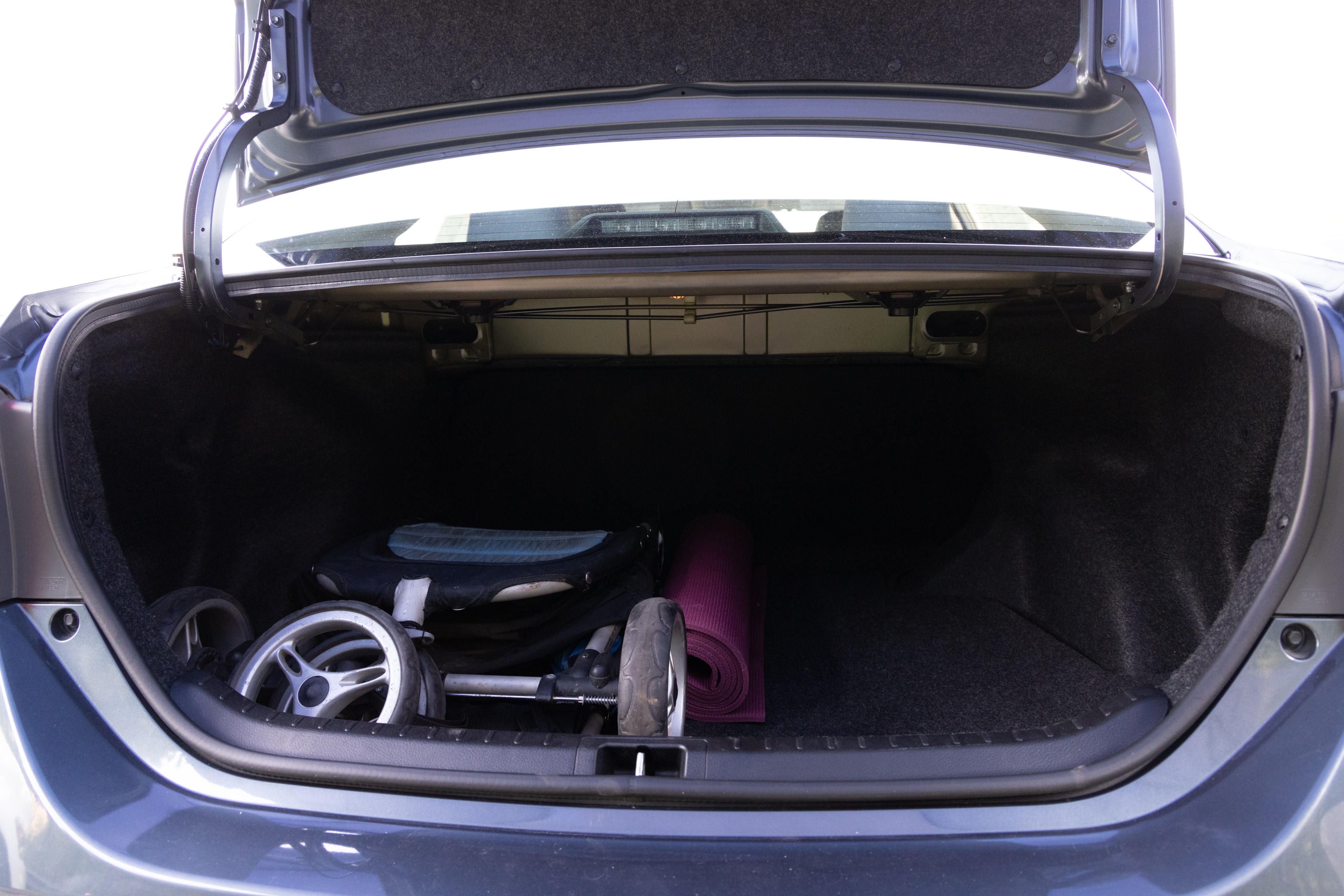 The trunk area is open giving a full view of the trunk area. A baby stroller, four grocery carriers, a yoga mat, and a set of golf clubs are placed inside.