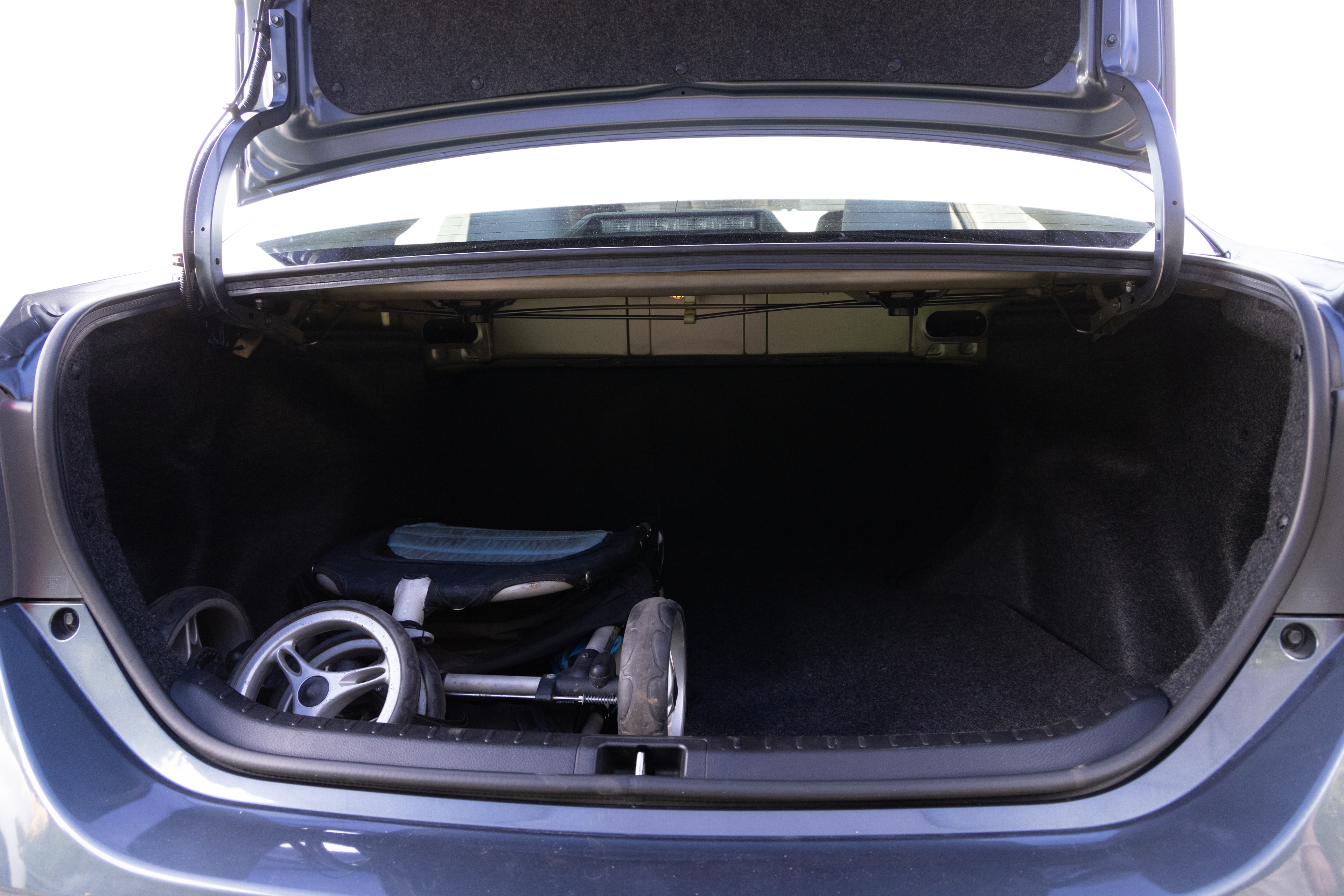 The trunk area is open giving a full view of the trunk area. A baby stroller, four grocery carriers, a yoga mat, and a set of golf clubs are placed inside.