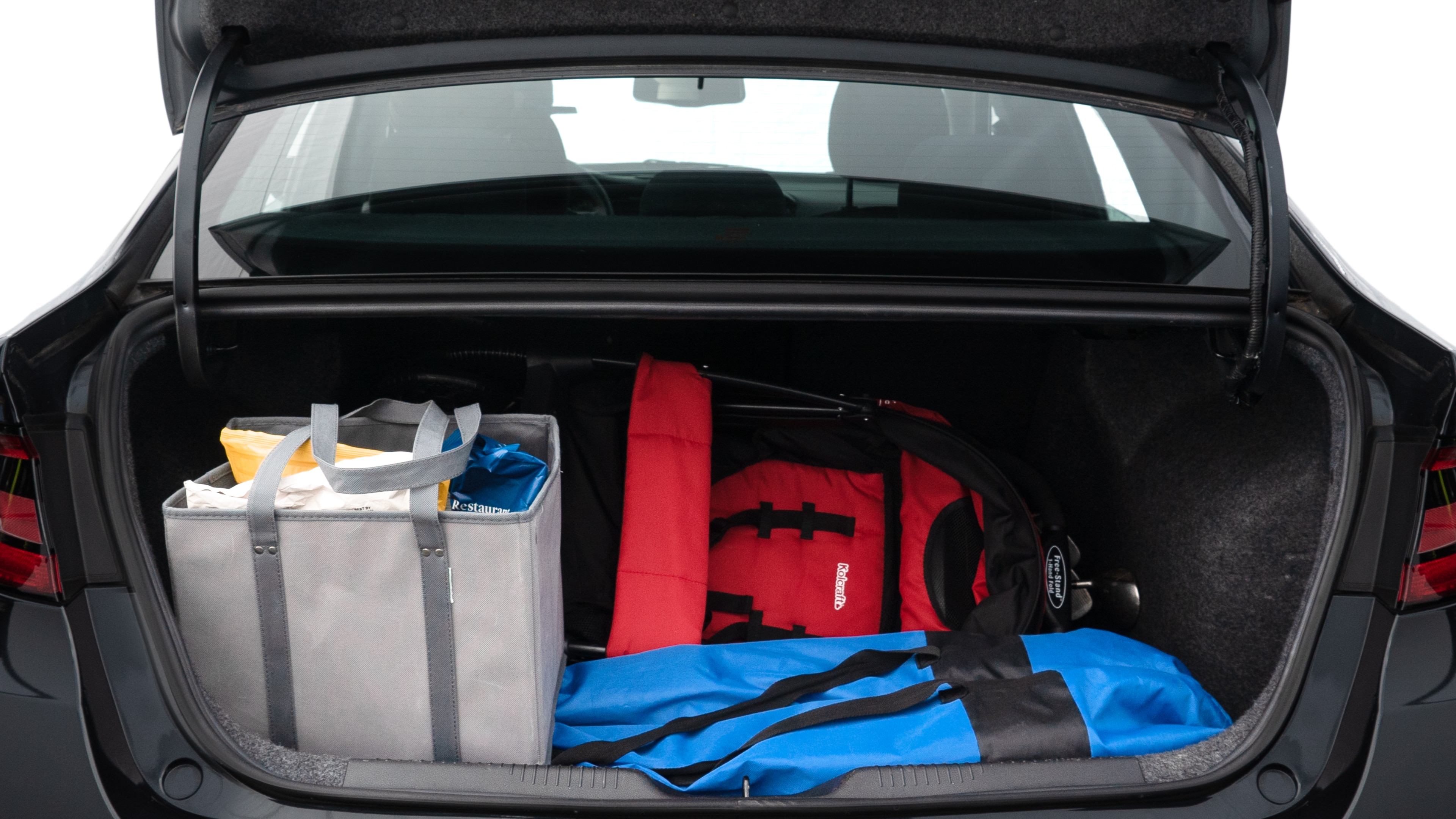 The trunk lid is open showing full view of the trunk. A baby stroller, three grocery carriers, two camping chairs in the carrying bag, and a set of golf clubs are placed inside.