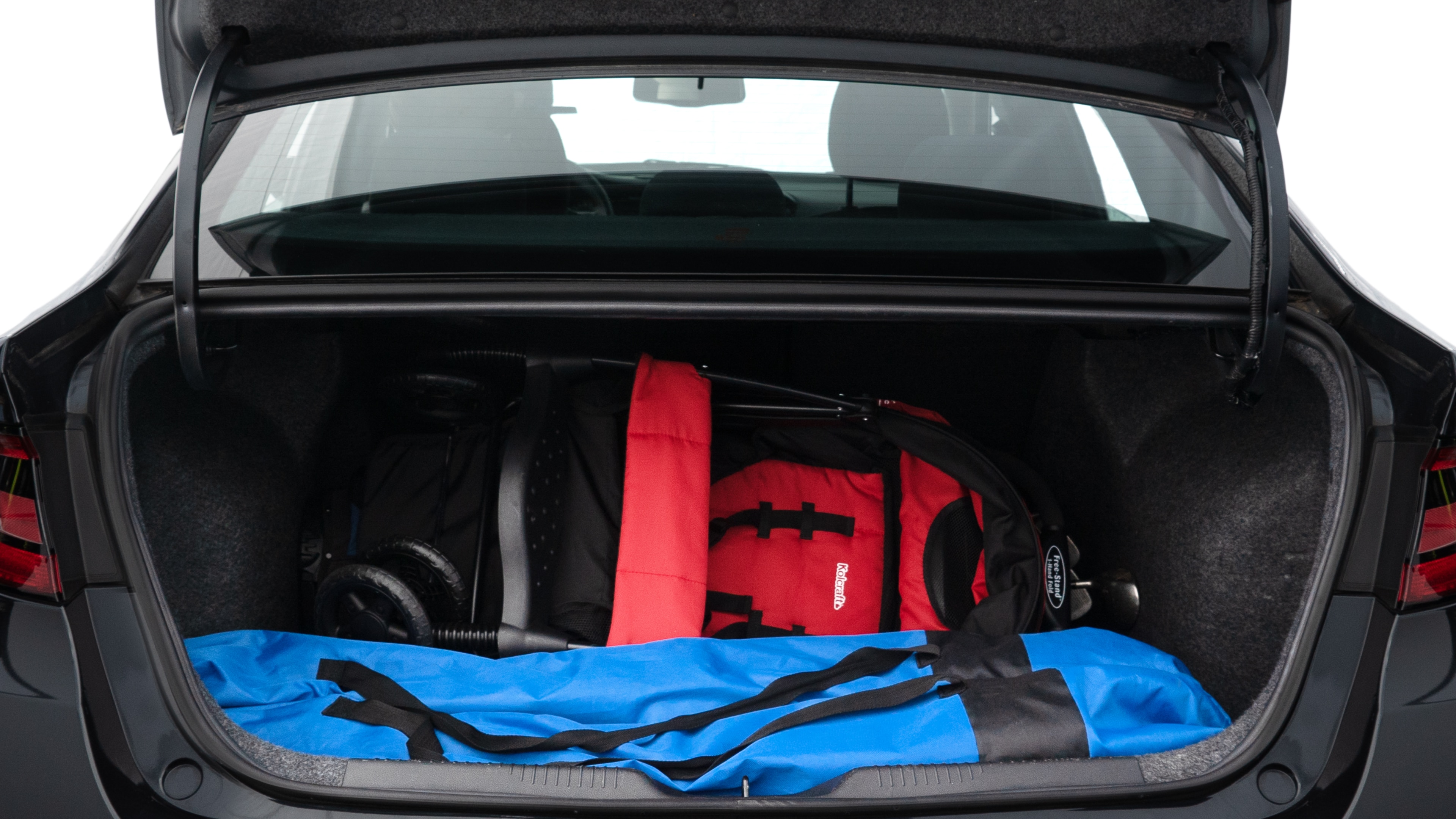 The trunk lid is open showing full view of the trunk. A baby stroller, three grocery carriers, two camping chairs in the carrying bag, and a set of golf clubs are placed inside.