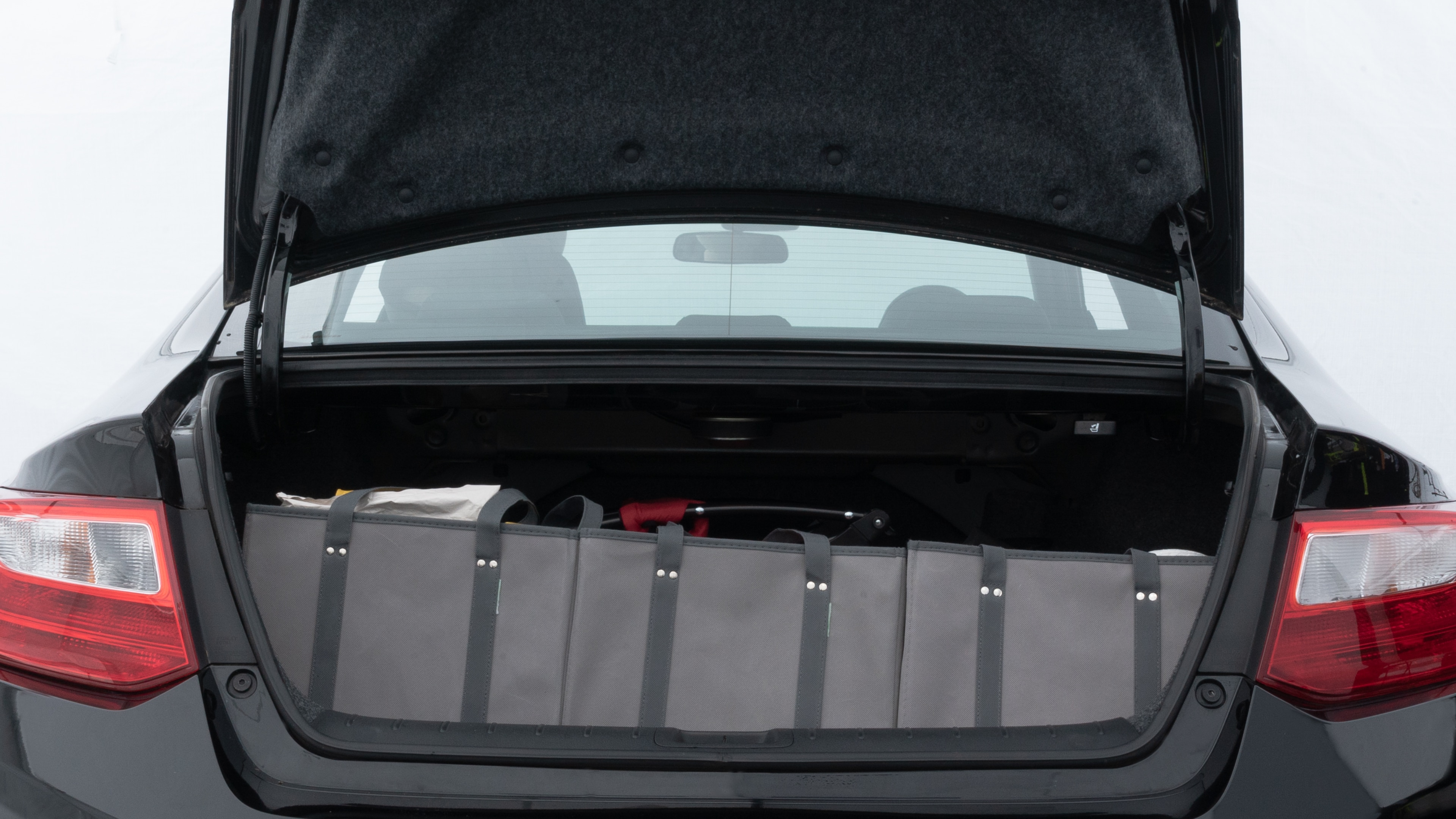 The trunk lid is open showing full view of the trunk. A baby stroller, three grocery carriers, two camping chairs in the carrying bag, and a set of golf clubs are placed inside.