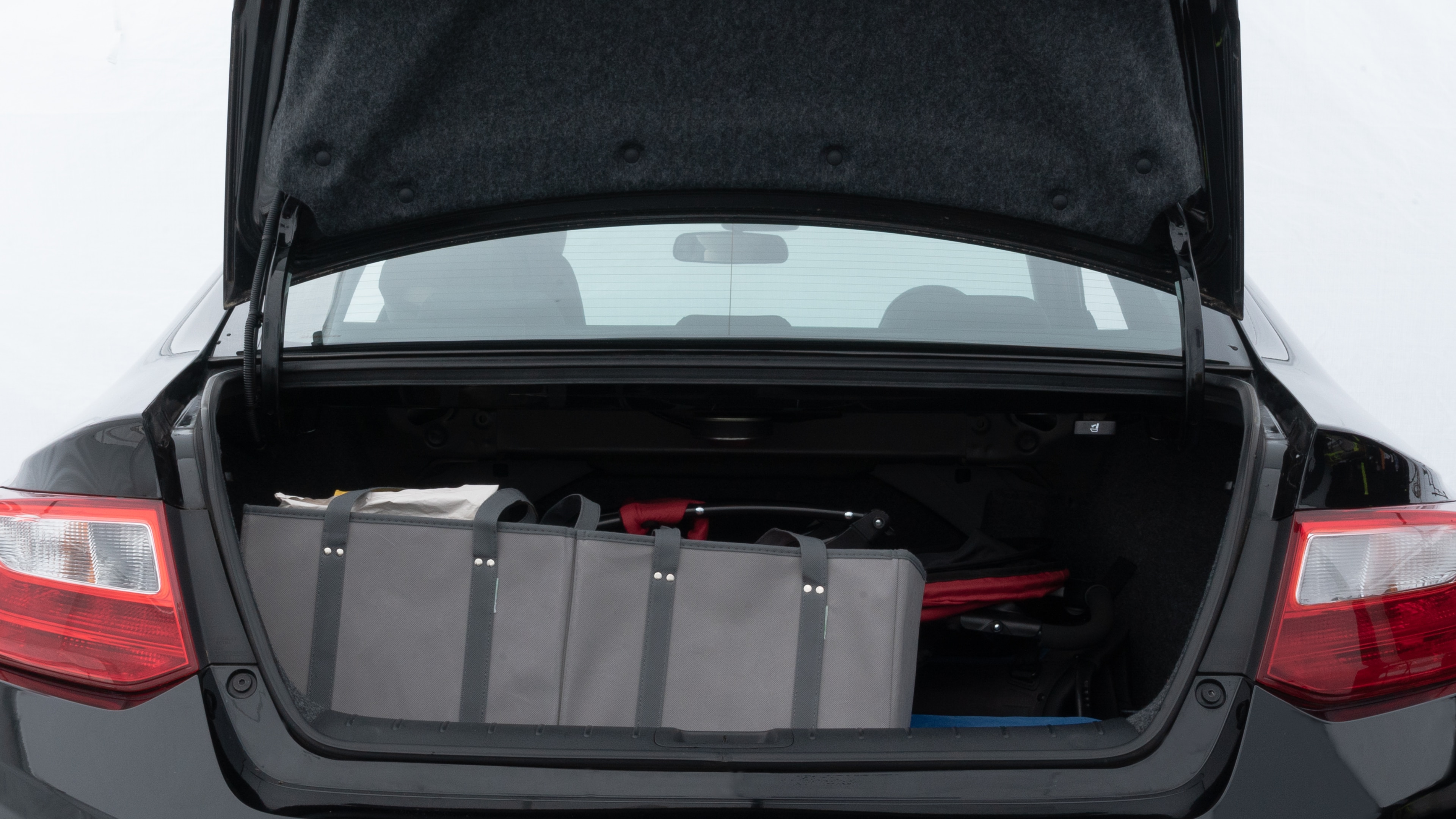 The trunk lid is open showing full view of the trunk. A baby stroller, three grocery carriers, two camping chairs in the carrying bag, and a set of golf clubs are placed inside.