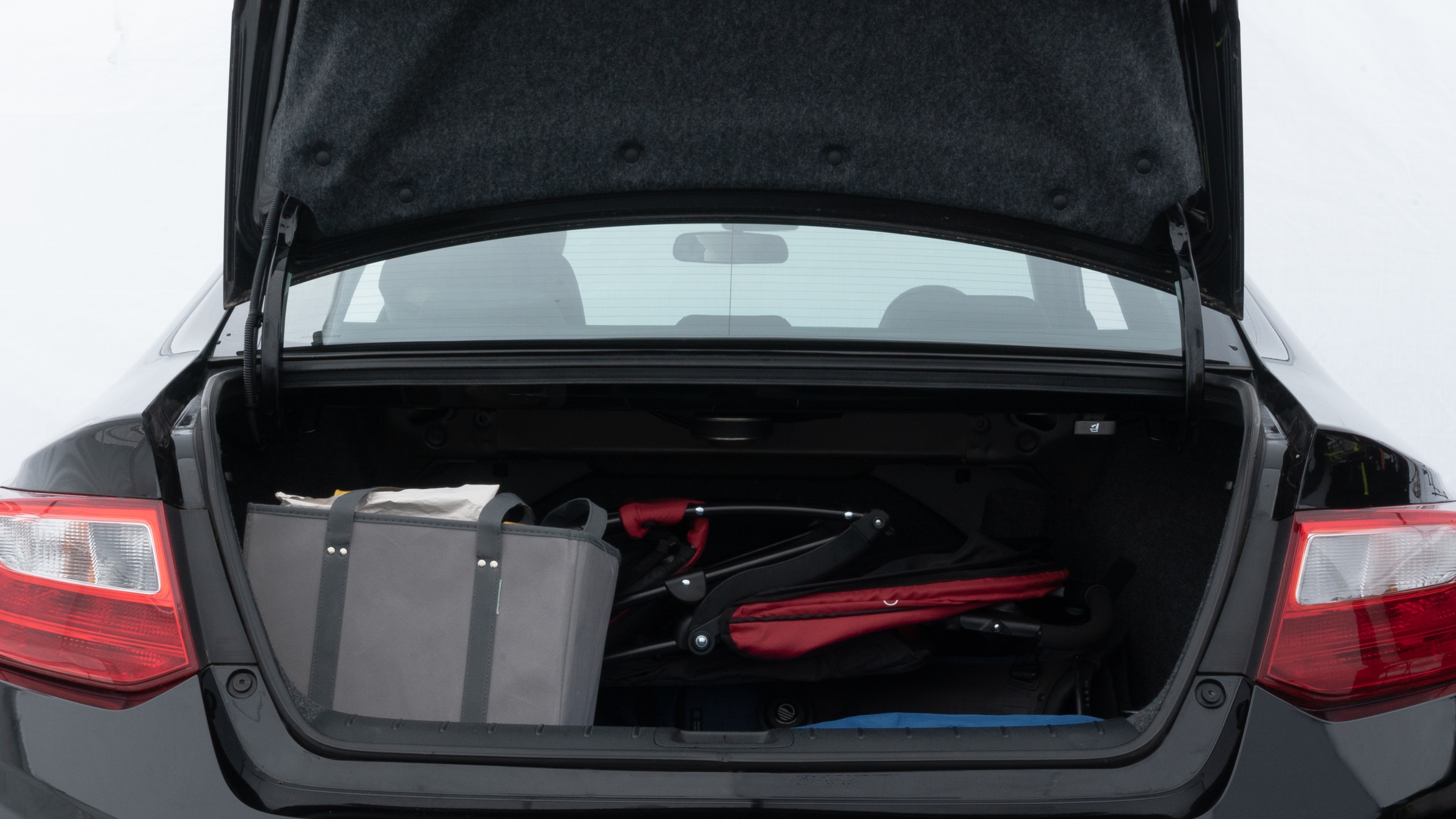 The trunk lid is open showing full view of the trunk. A baby stroller, three grocery carriers, two camping chairs in the carrying bag, and a set of golf clubs are placed inside.
