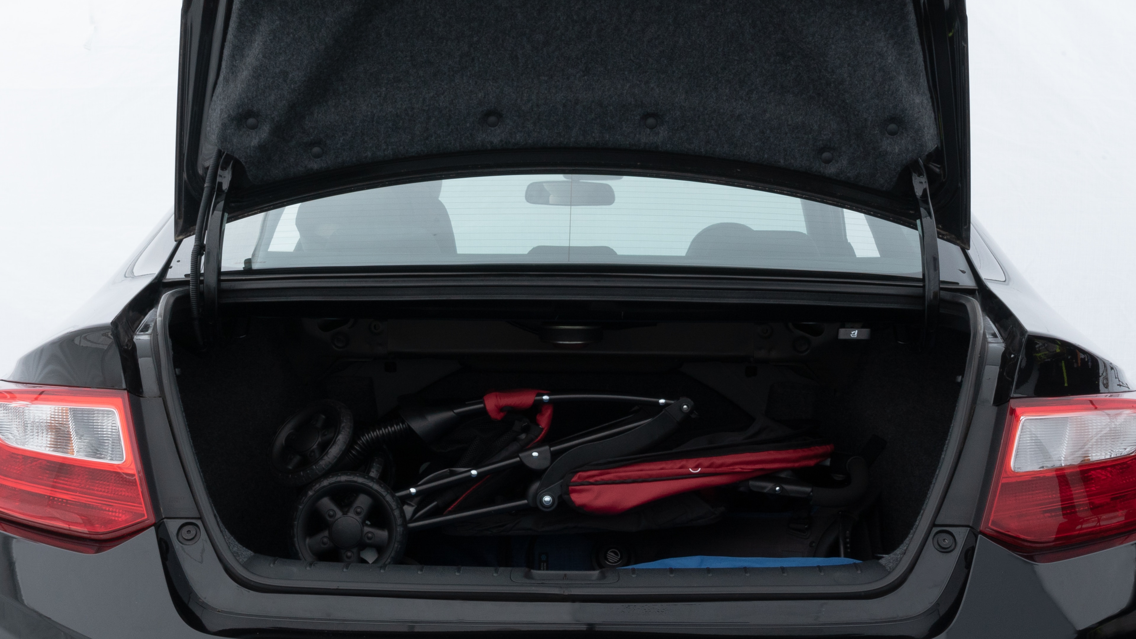 The trunk lid is open showing full view of the trunk. A baby stroller, three grocery carriers, two camping chairs in the carrying bag, and a set of golf clubs are placed inside.