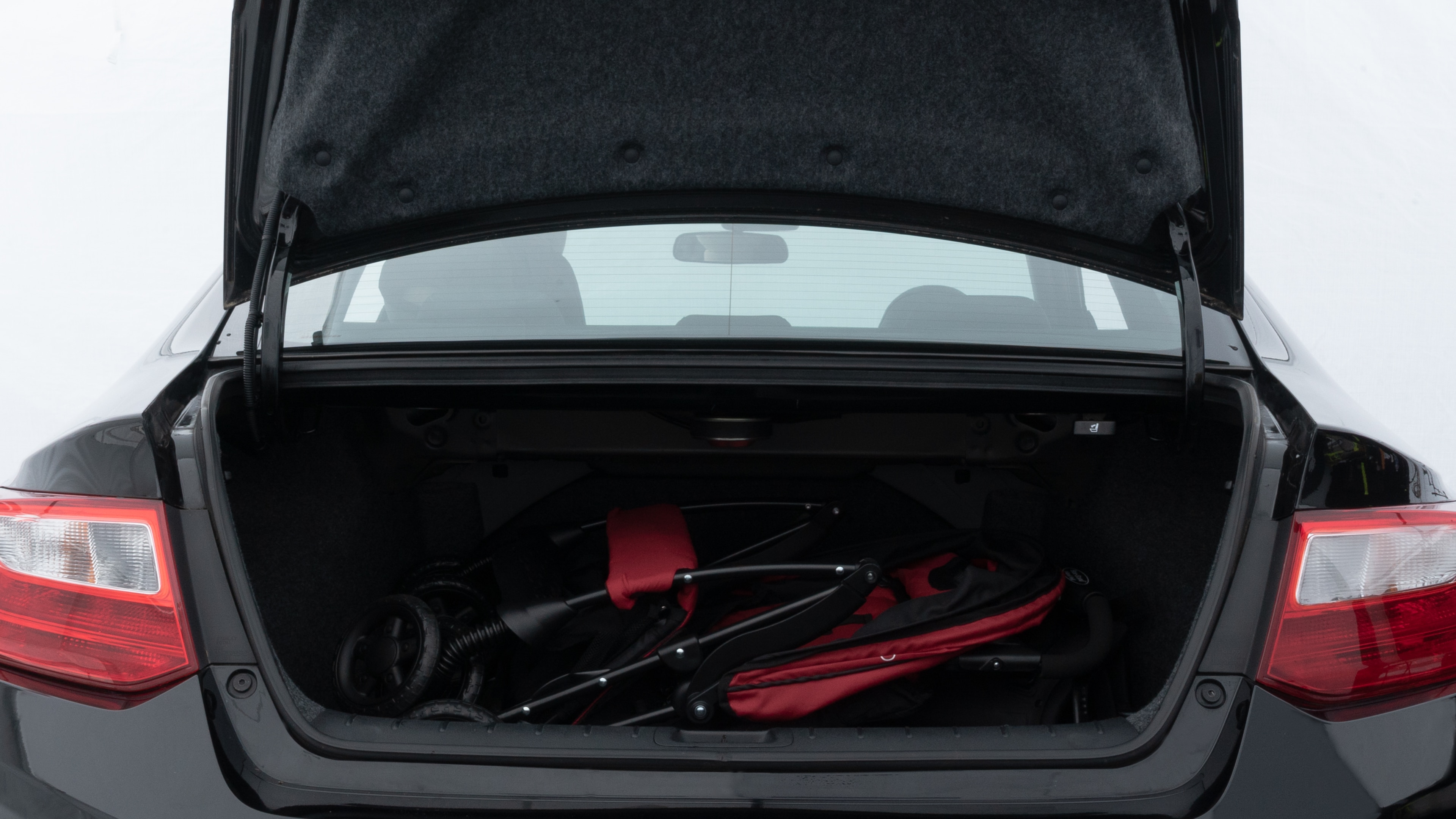 The trunk lid is open showing full view of the trunk. A baby stroller, three grocery carriers, two camping chairs in the carrying bag, and a set of golf clubs are placed inside.