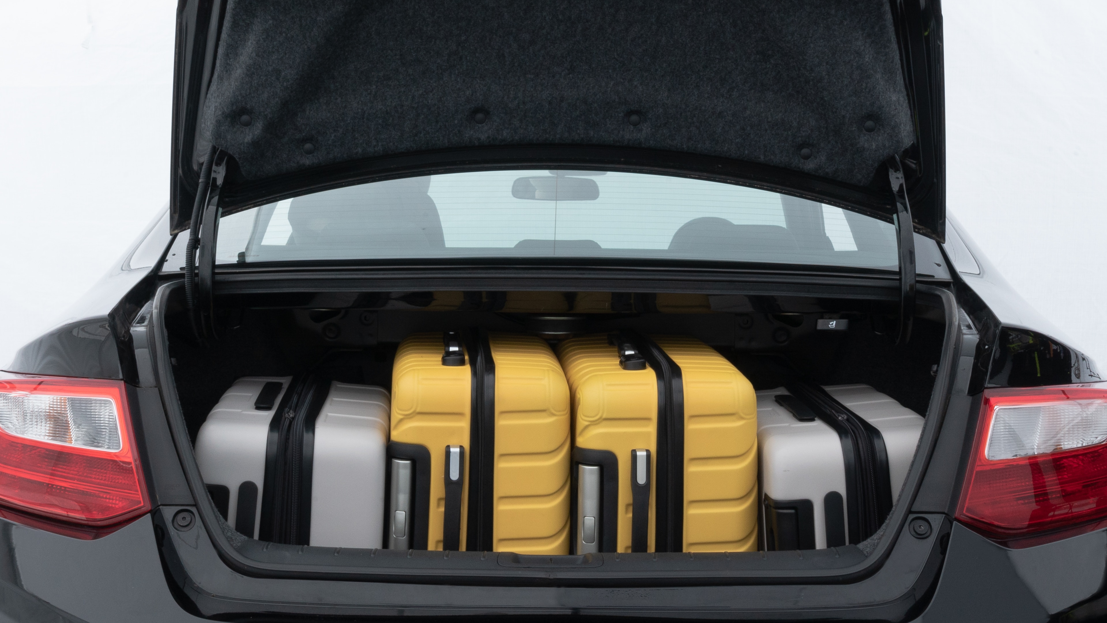 The trunk lid is open, showing full view of the trunk space. Two medium and two small suitcases are placed inside.