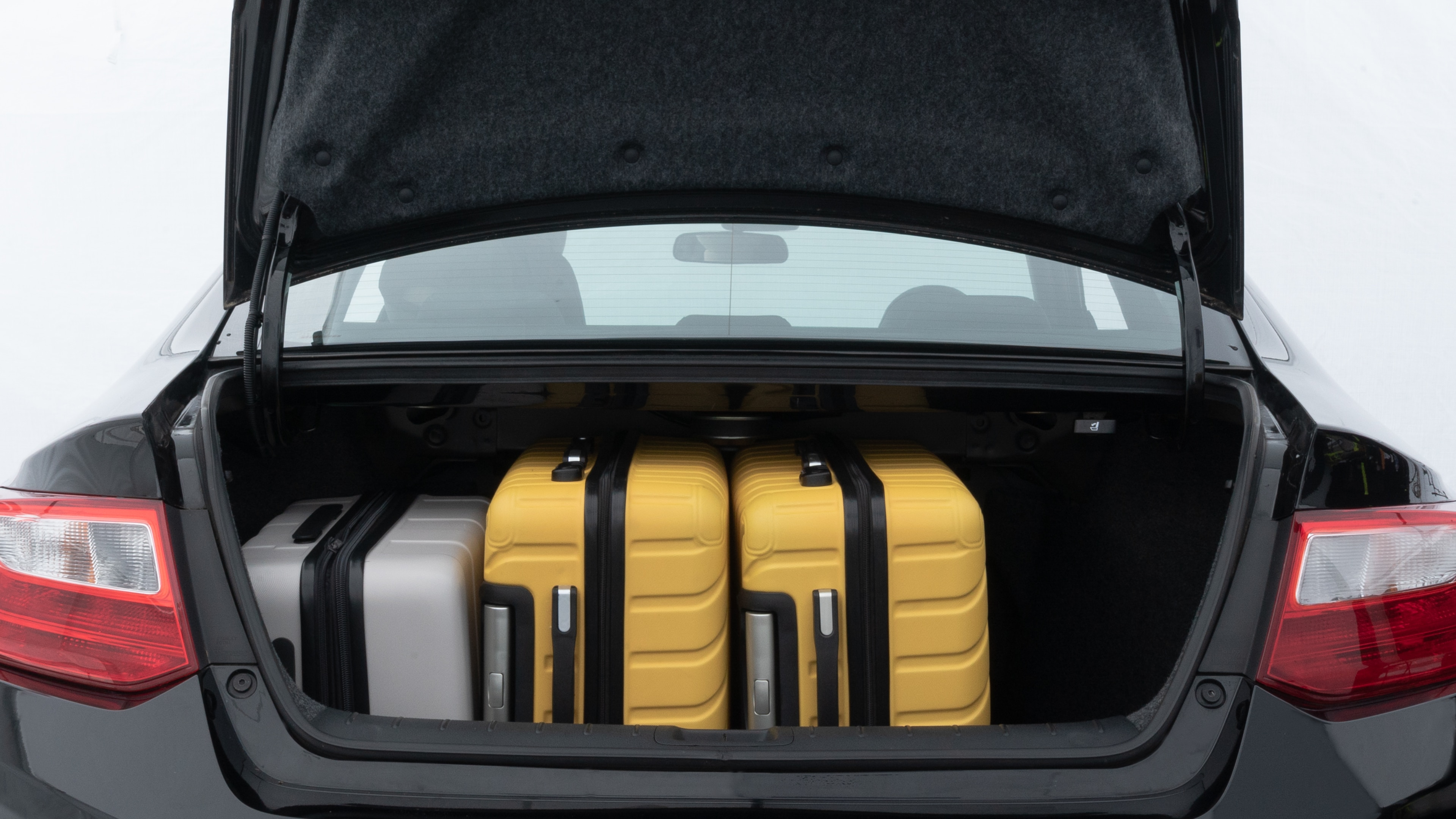 The trunk lid is open, showing full view of the trunk space. Two medium and two small suitcases are placed inside.