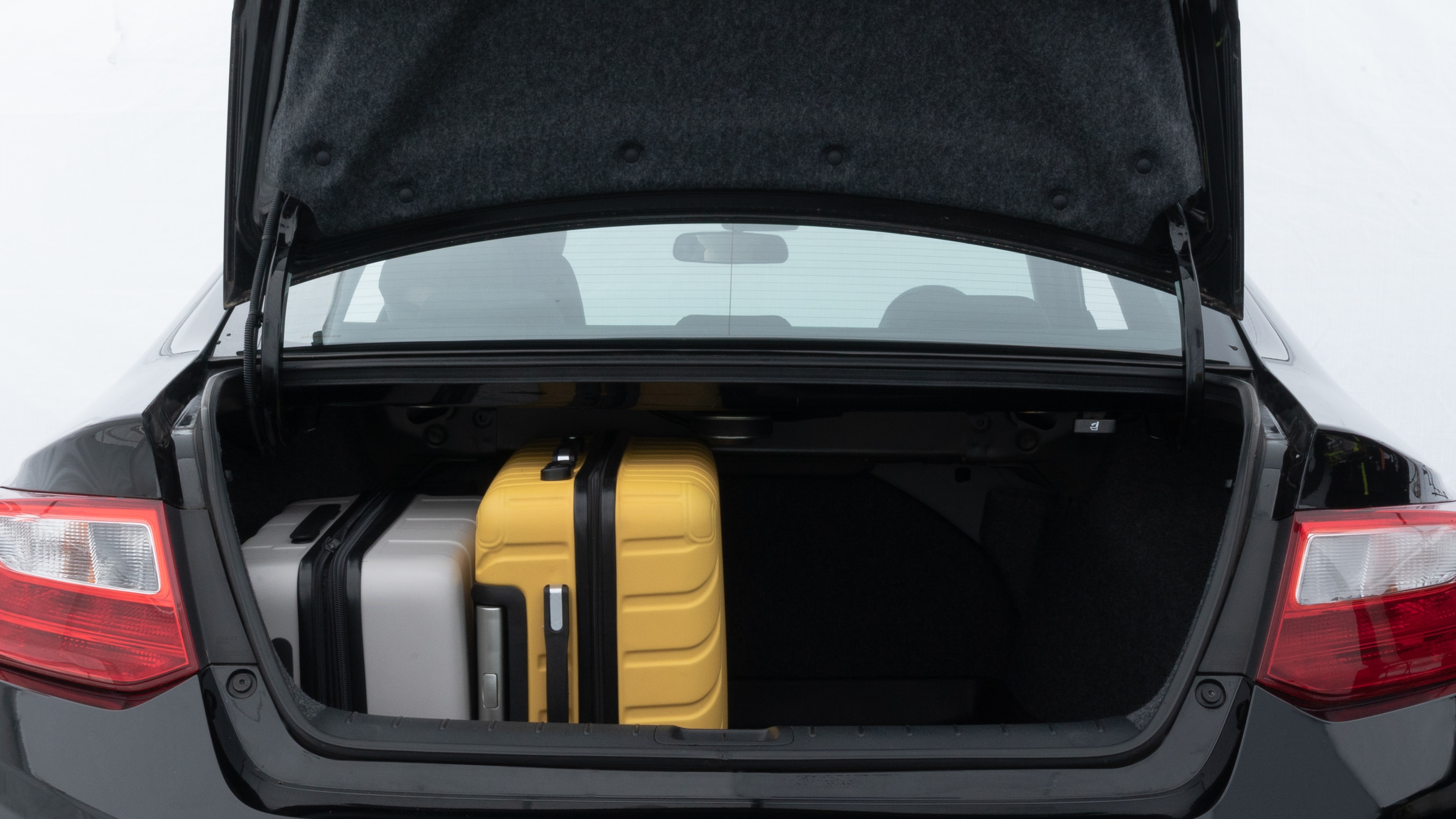 The trunk lid is open, showing full view of the trunk space. Two medium and two small suitcases are placed inside.