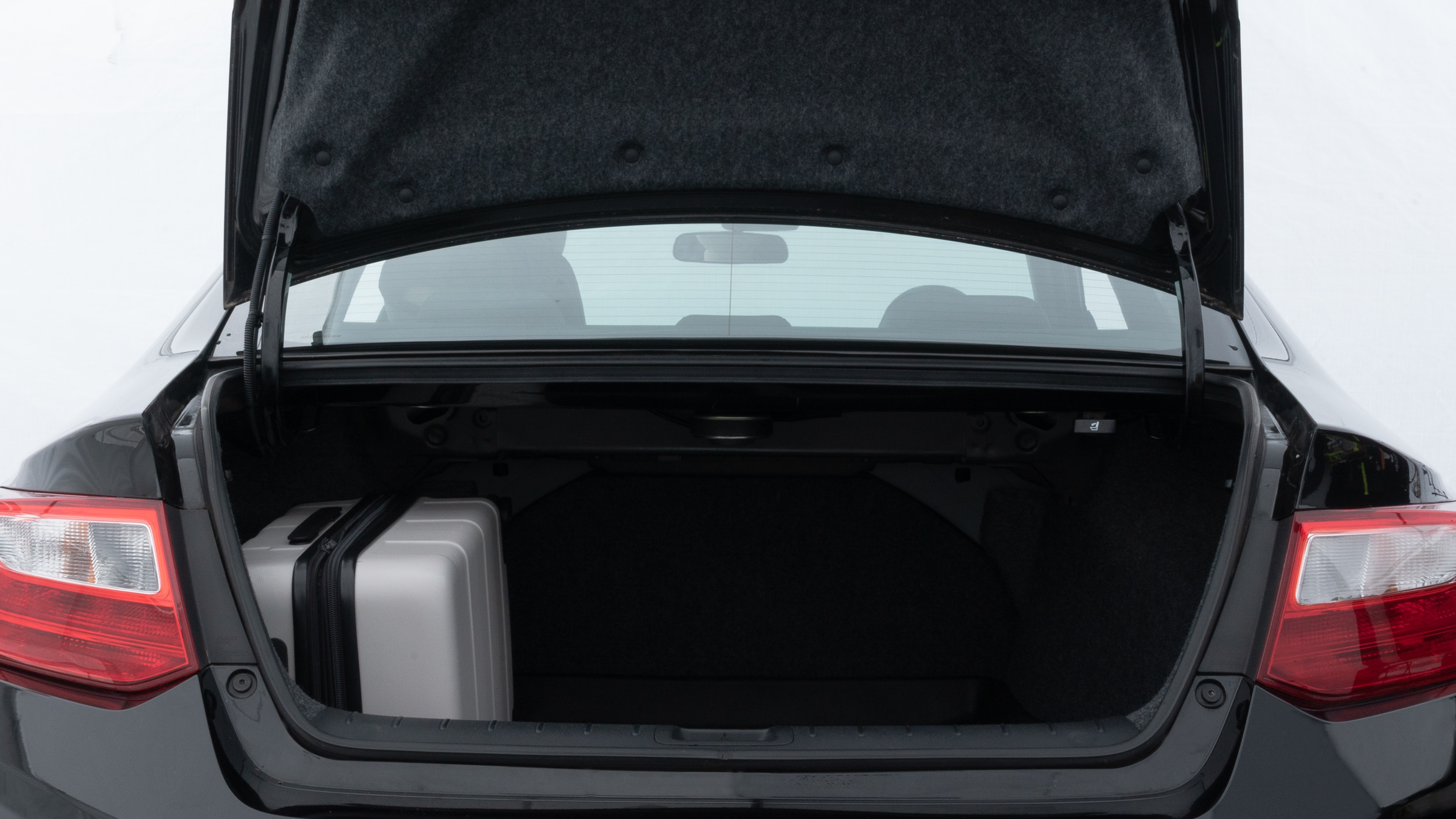 The trunk lid is open, showing full view of the trunk space. Two medium and two small suitcases are placed inside.