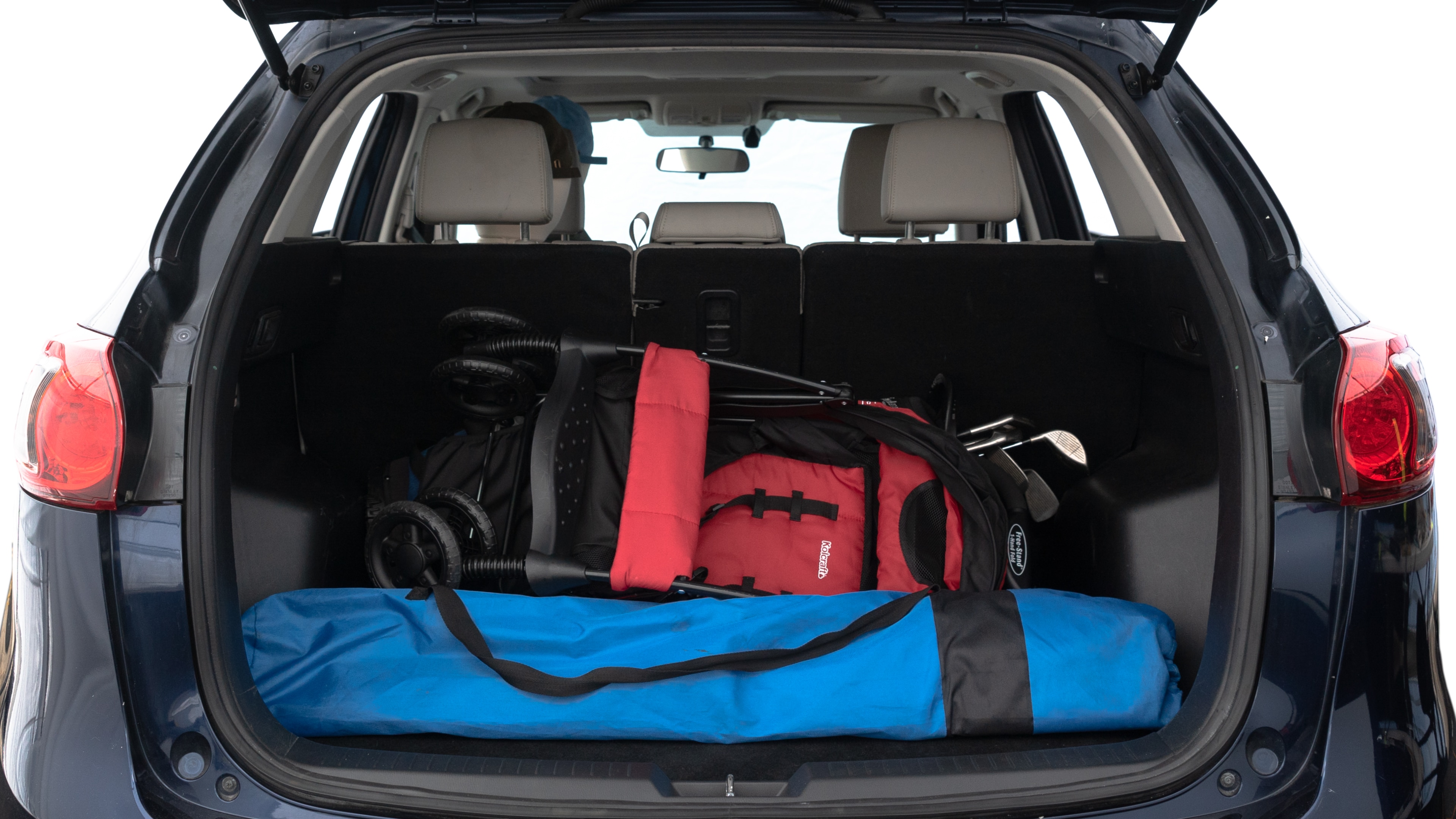 The trunk lid is open showing full view of the trunk. A baby stroller, three grocery carriers, two camping chairs in the carrying bag, and a set of golf clubs are placed inside.