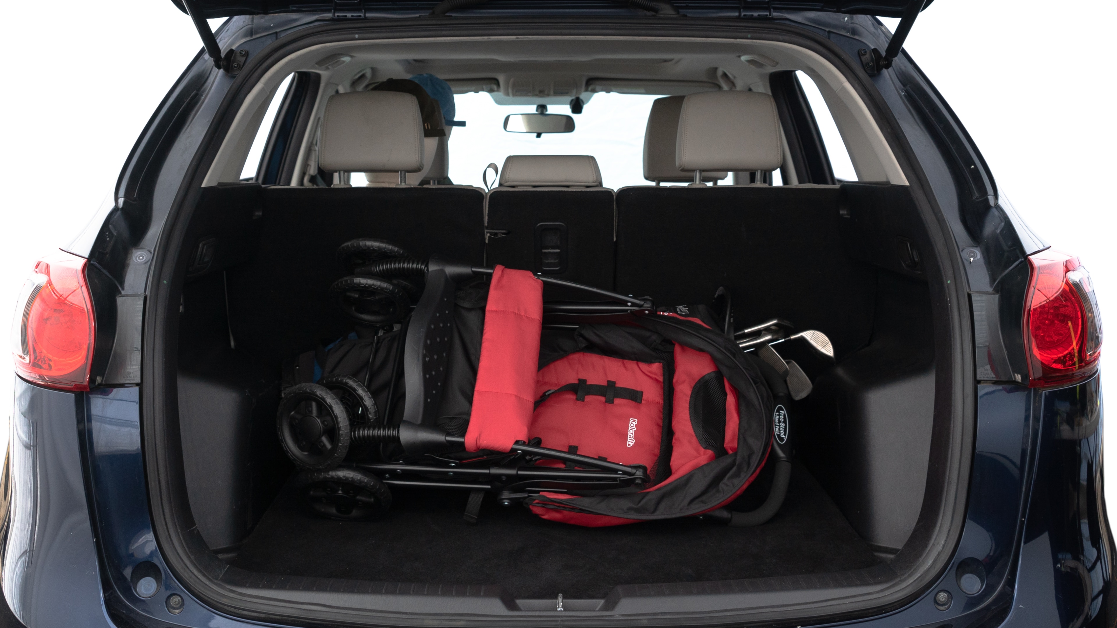 The trunk lid is open showing full view of the trunk. A baby stroller, three grocery carriers, two camping chairs in the carrying bag, and a set of golf clubs are placed inside.