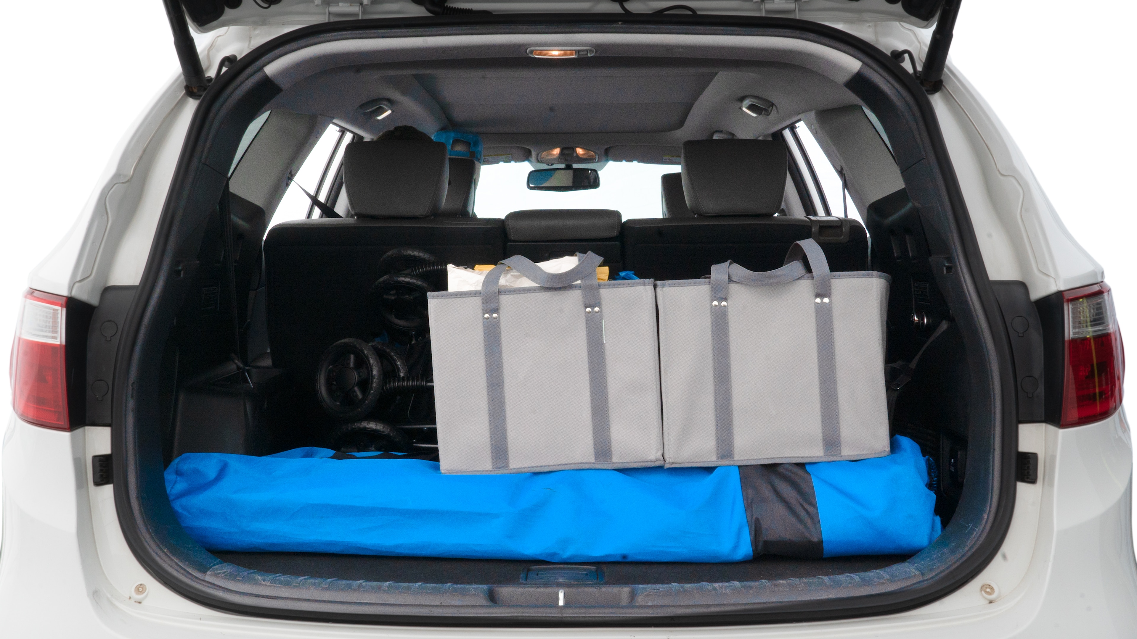 The trunk lid is open showing full view of the trunk. A baby stroller, three grocery carriers, two camping chairs in the carrying bag, and a set of golf clubs are placed inside.