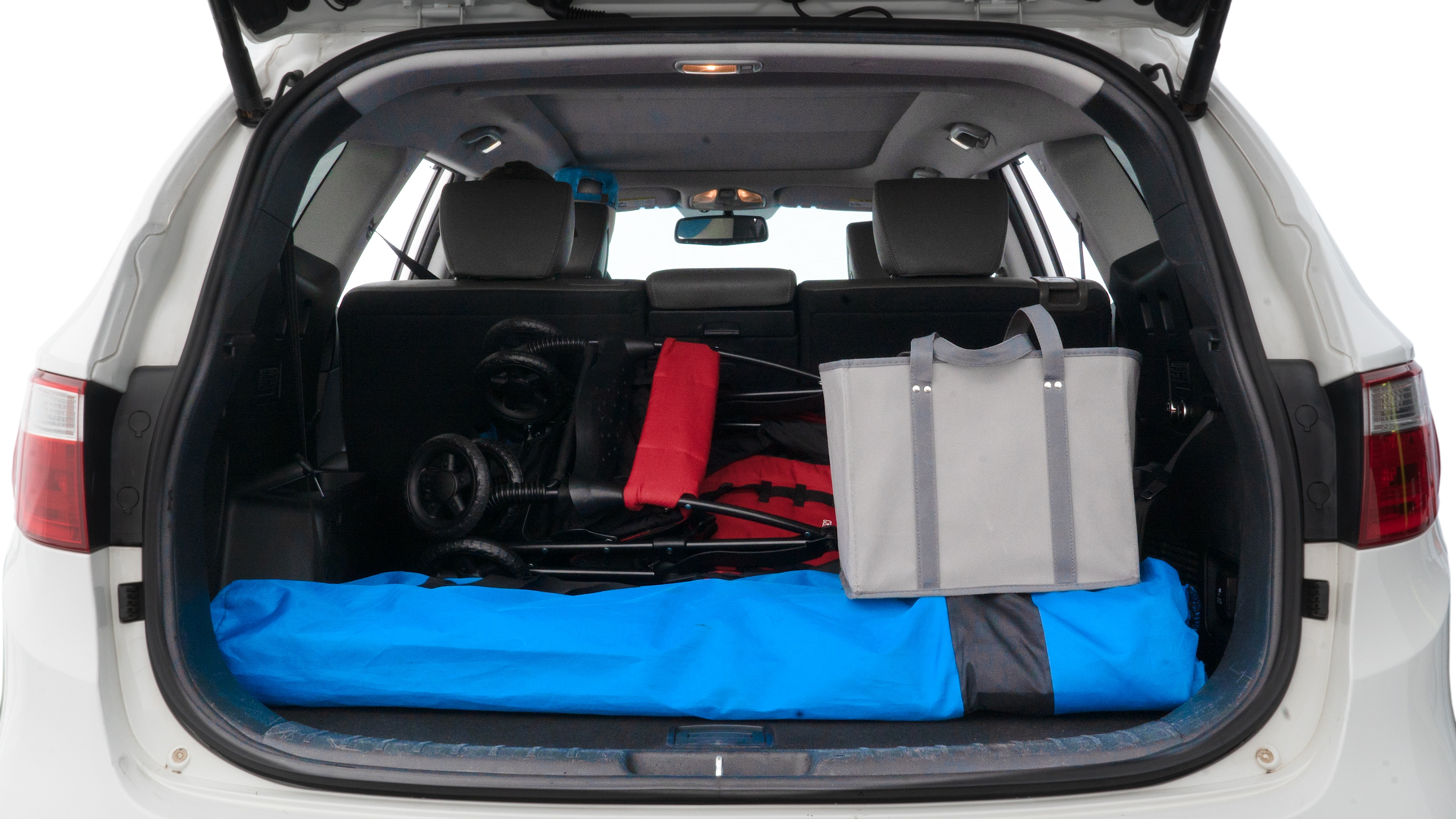 The trunk lid is open showing full view of the trunk. A baby stroller, three grocery carriers, two camping chairs in the carrying bag, and a set of golf clubs are placed inside.