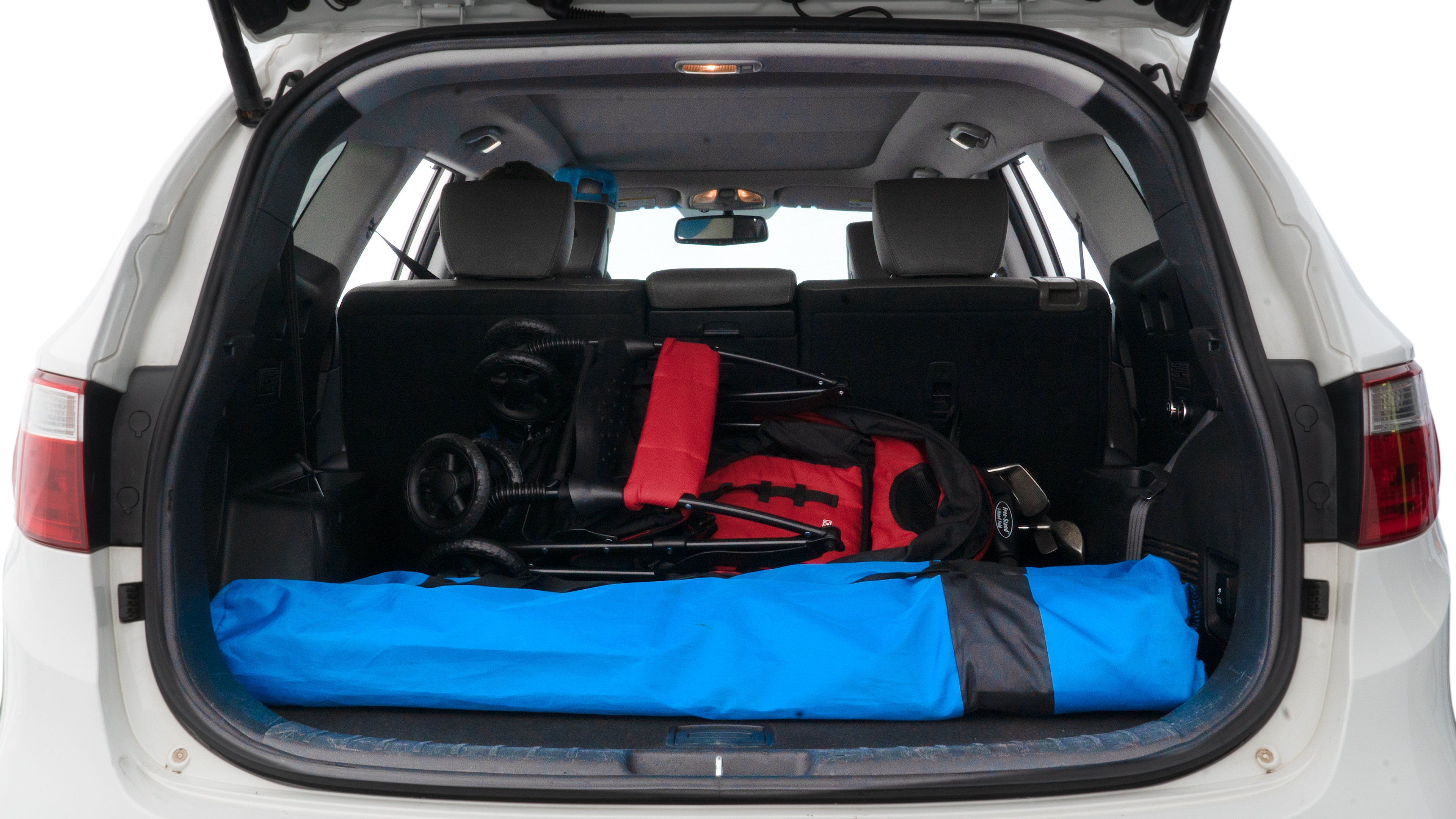 The trunk lid is open showing full view of the trunk. A baby stroller, three grocery carriers, two camping chairs in the carrying bag, and a set of golf clubs are placed inside.