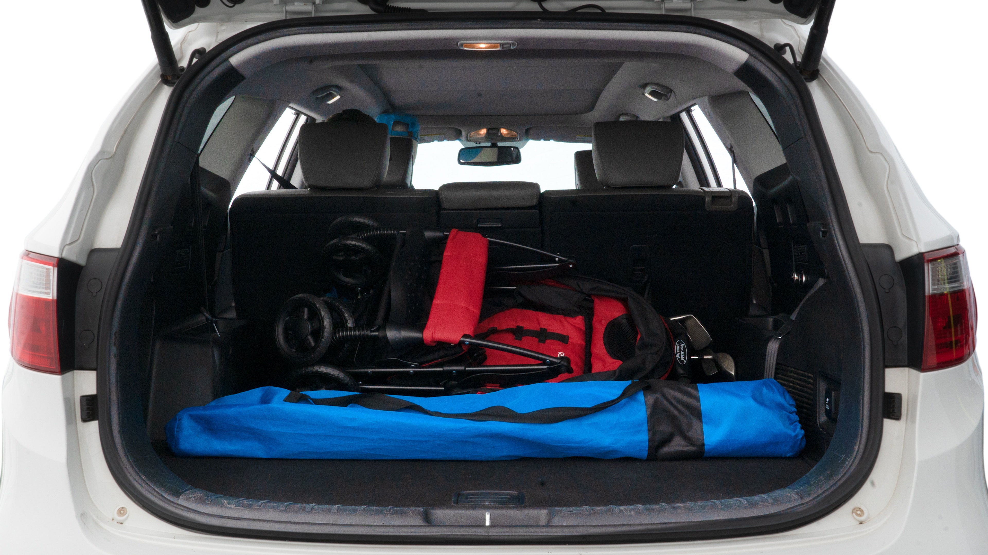 The trunk lid is open showing full view of the trunk. A baby stroller, three grocery carriers, two camping chairs in the carrying bag, and a set of golf clubs are placed inside.
