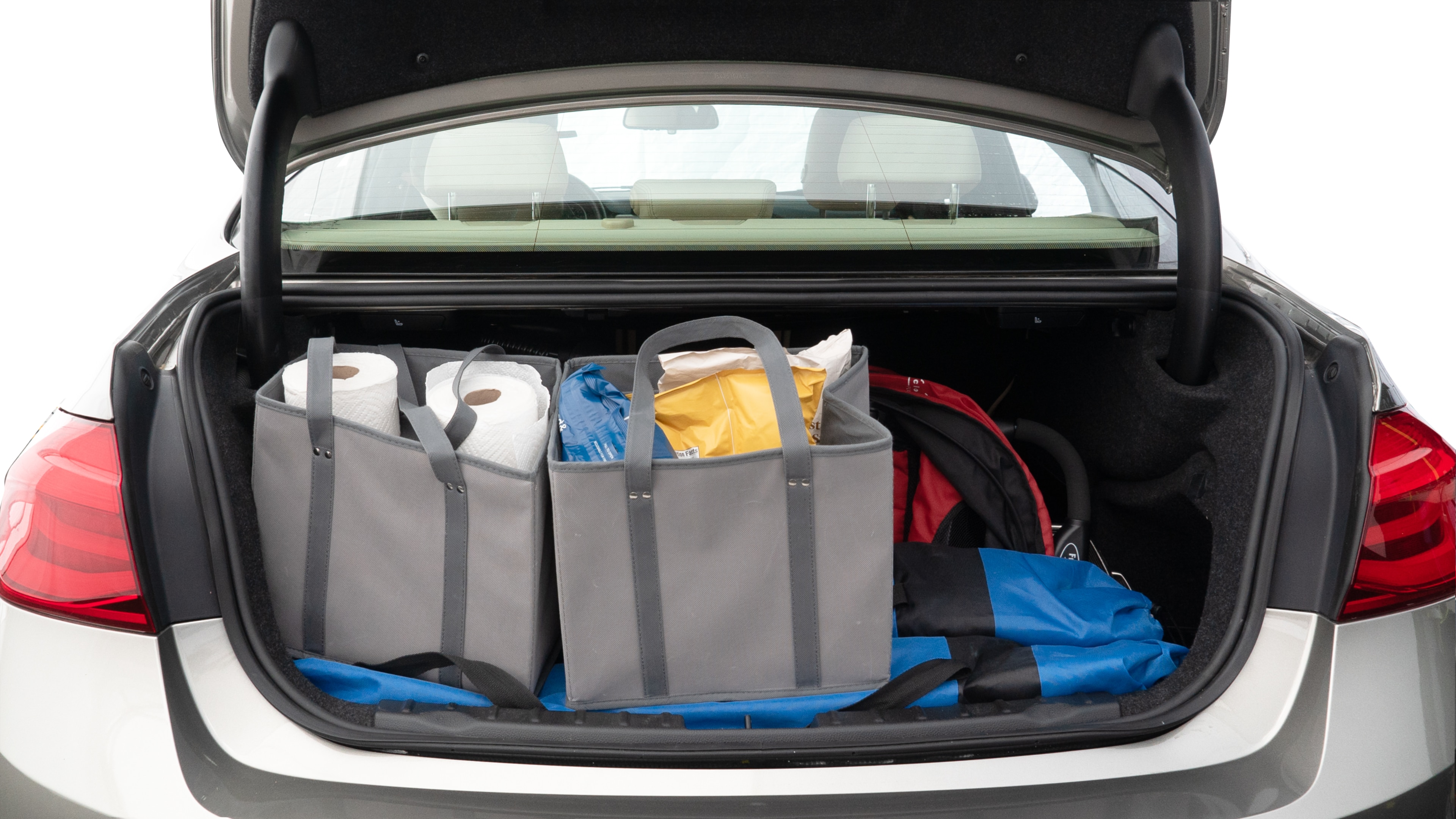 The trunk lid is open showing full view of the trunk. A baby stroller, three grocery carriers, two camping chairs in the carrying bag, and a set of golf clubs are placed inside.