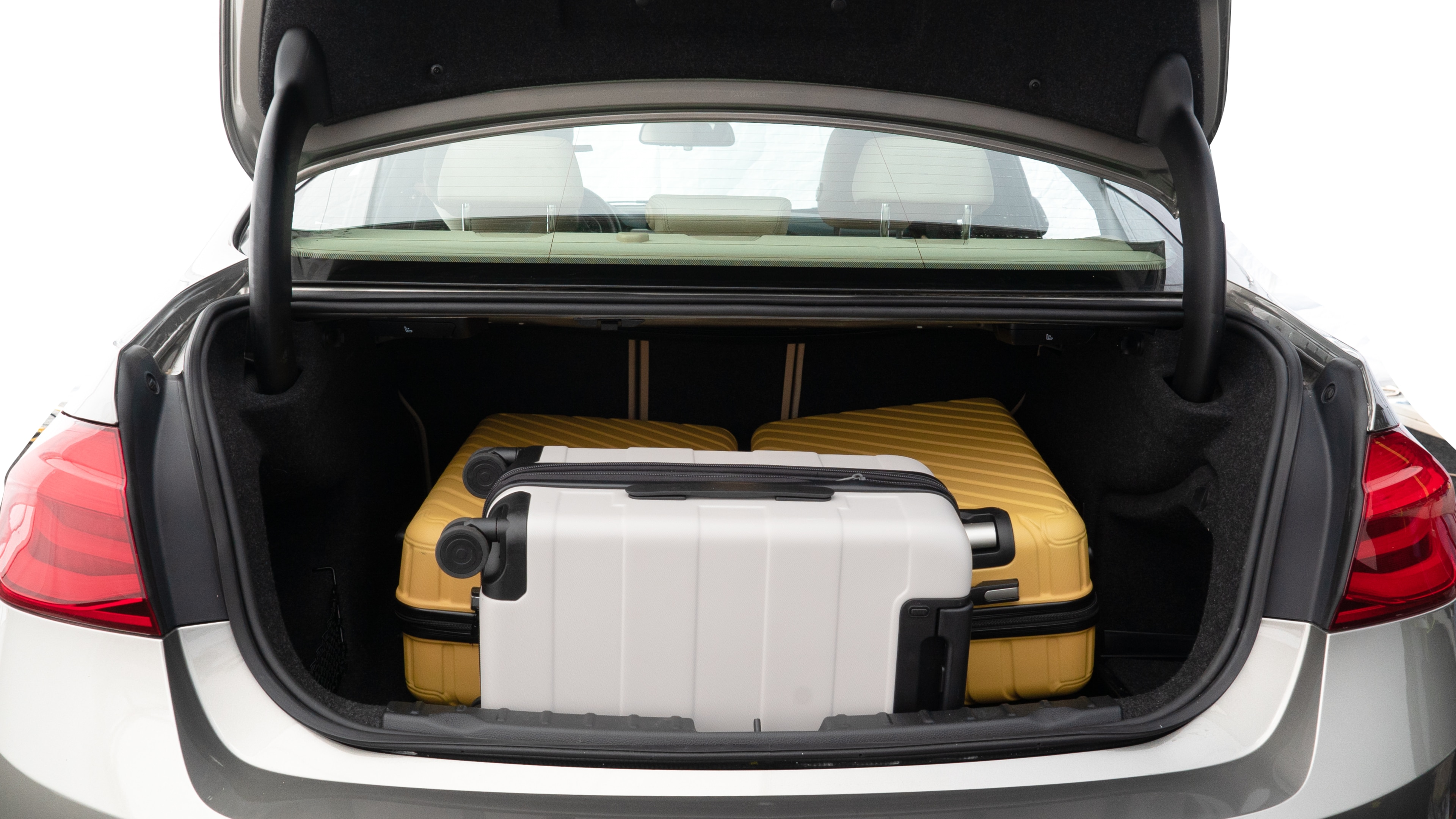 The trunk lid is open, showing full view of the trunk space. Two medium and one small suitcase are placed inside.
