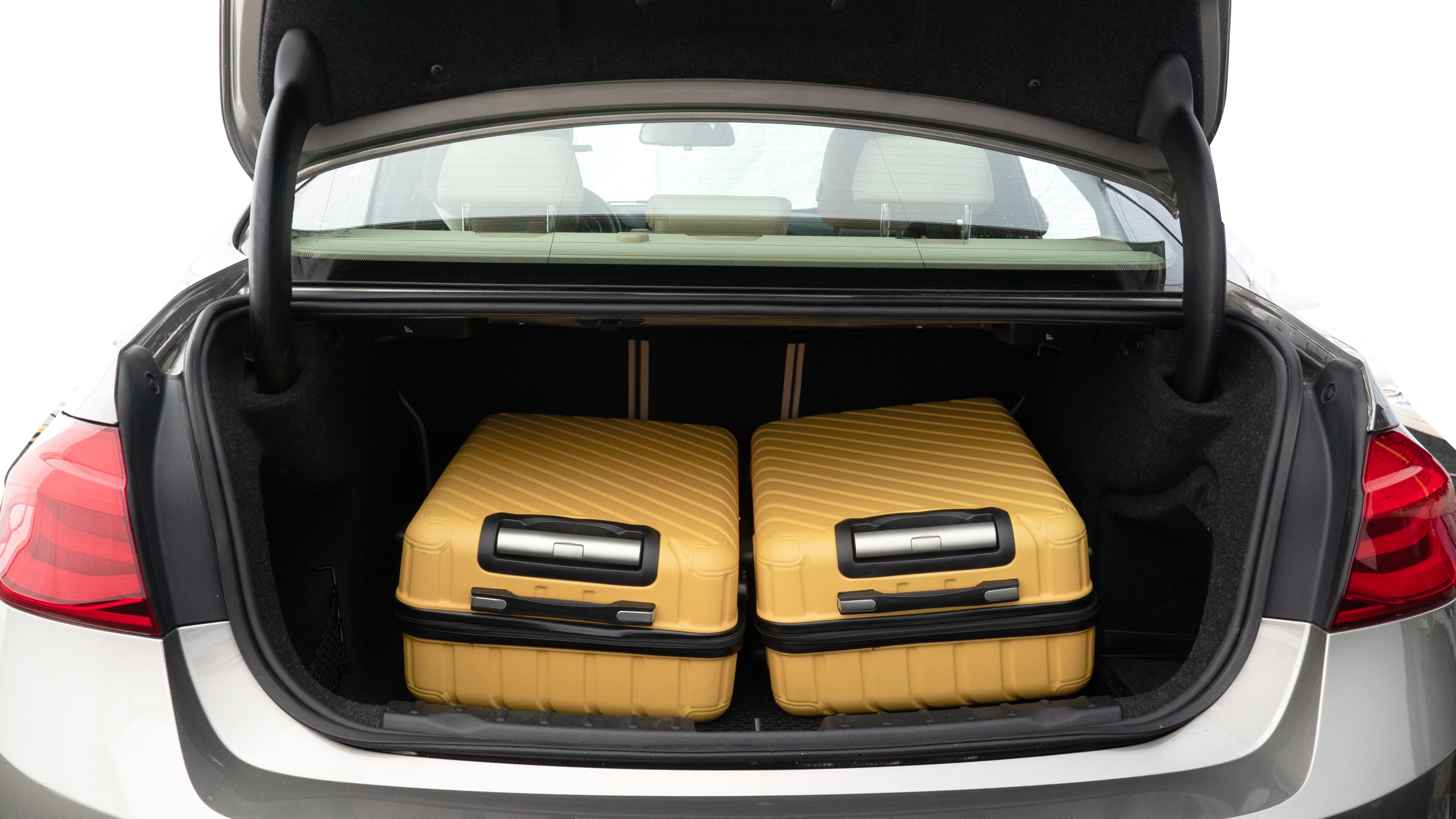 The trunk lid is open, showing full view of the trunk space. Two medium and one small suitcase are placed inside.