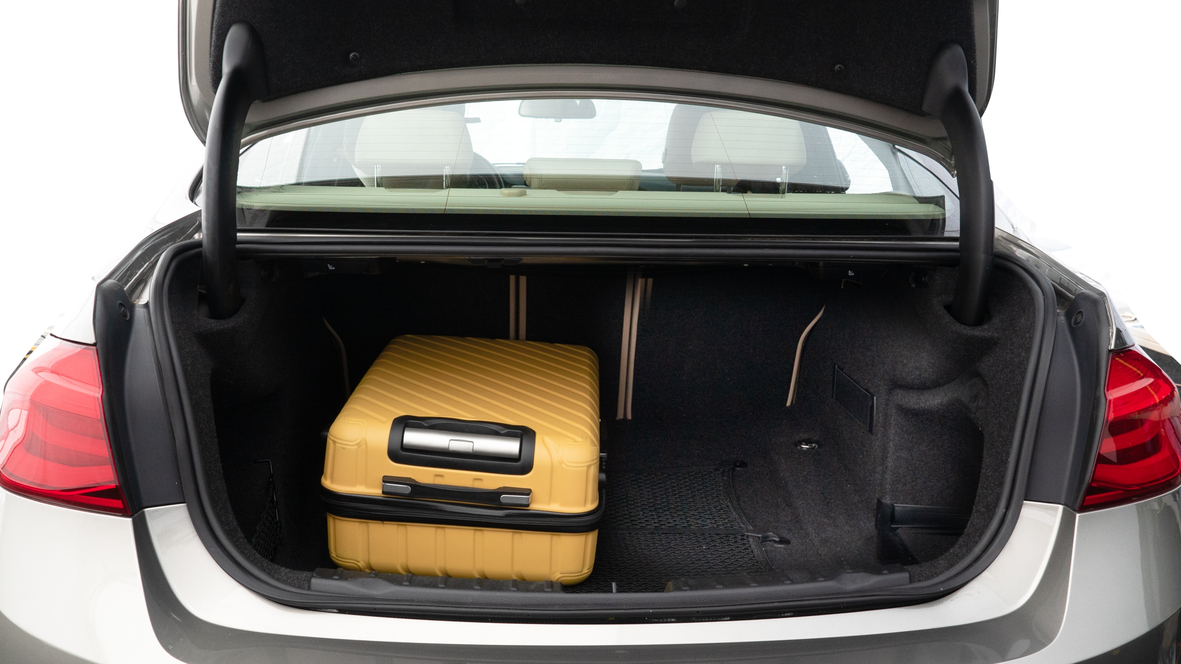 The trunk lid is open, showing full view of the trunk space. Two medium and one small suitcase are placed inside.