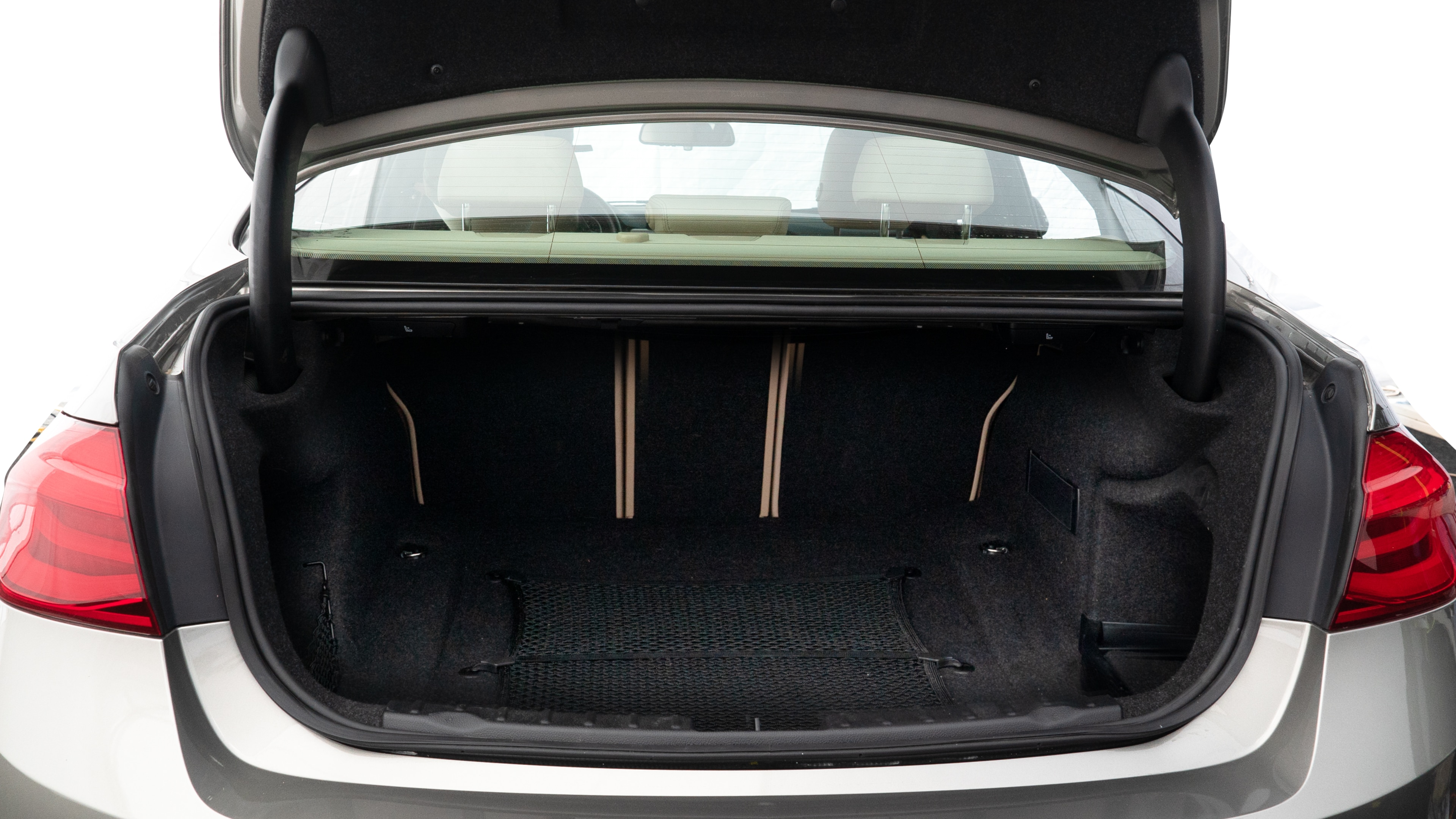 The trunk lid is open, showing full view of the trunk space. Two medium and one small suitcase are placed inside.