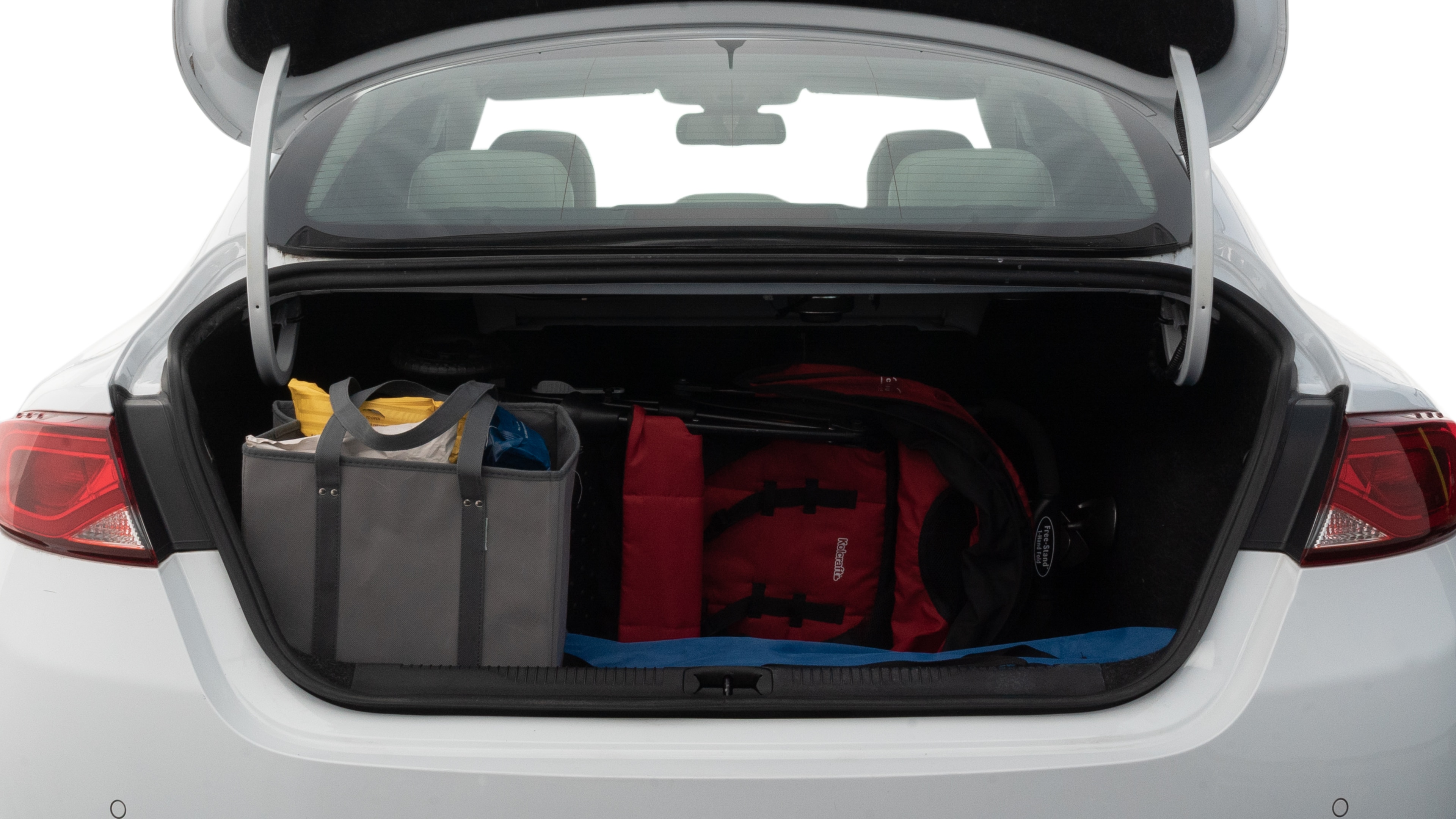 The trunk lid is open showing full view of the trunk. A baby stroller, three grocery carriers, two camping chairs in the carrying bag, and a set of golf clubs are placed inside.