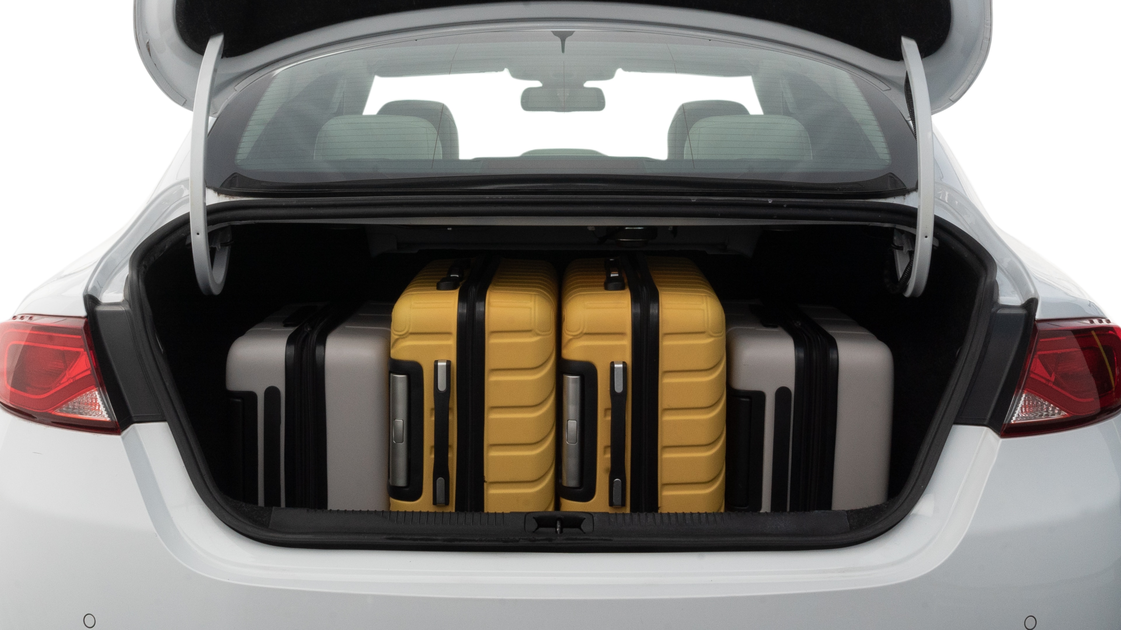 The trunk lid is open, showing full view of the trunk space. Two medium and two small suitcases are placed inside.