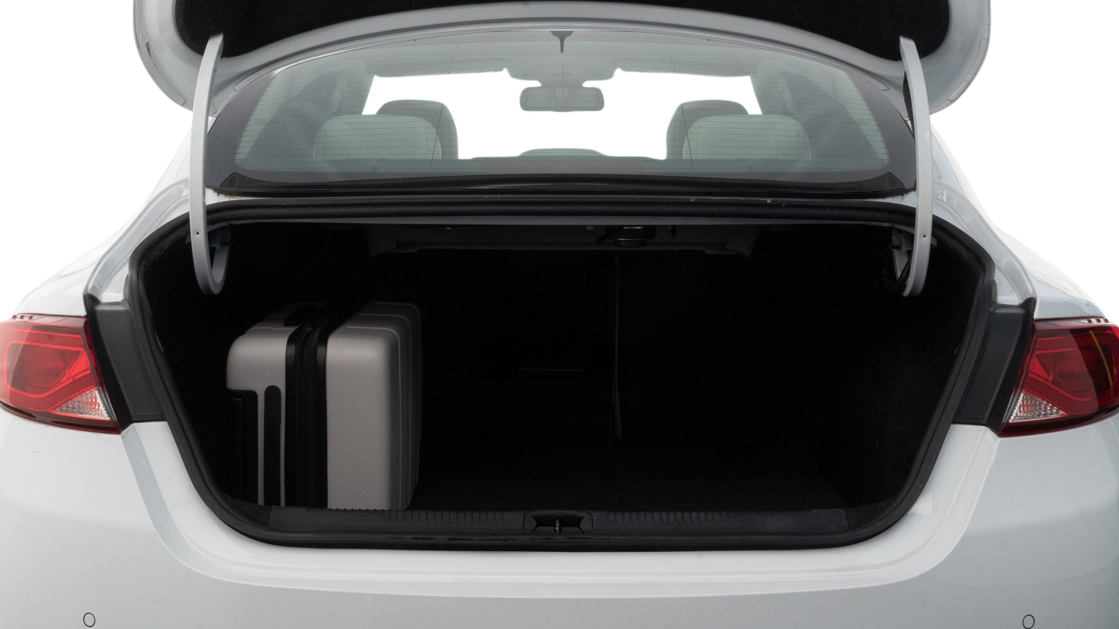 The trunk lid is open, showing full view of the trunk space. Two medium and two small suitcases are placed inside.