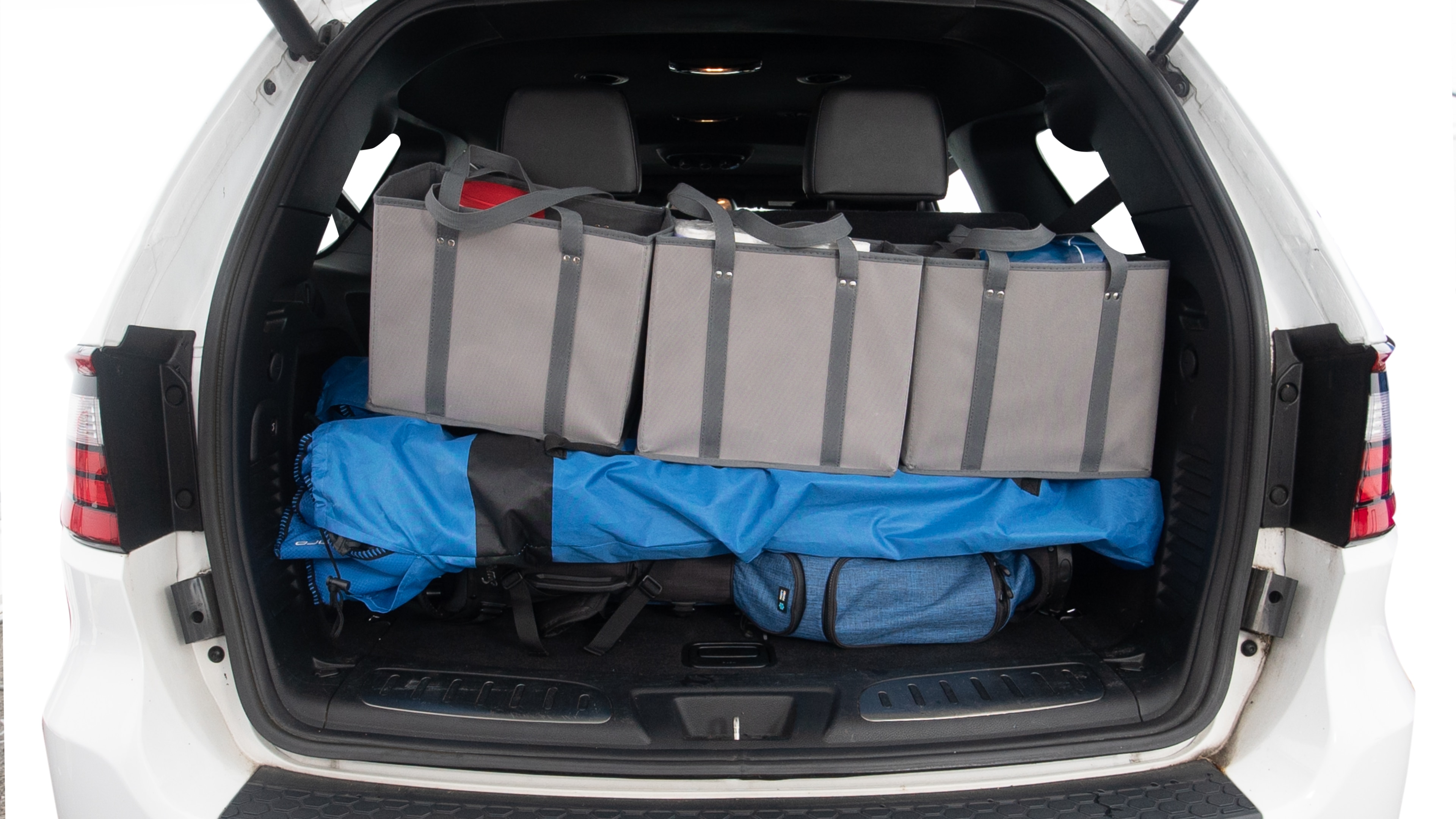 The trunk lid is open showing full view of the trunk. Three grocery carriers, two camping chairs in the carrying bag, and a set of golf clubs are placed inside.