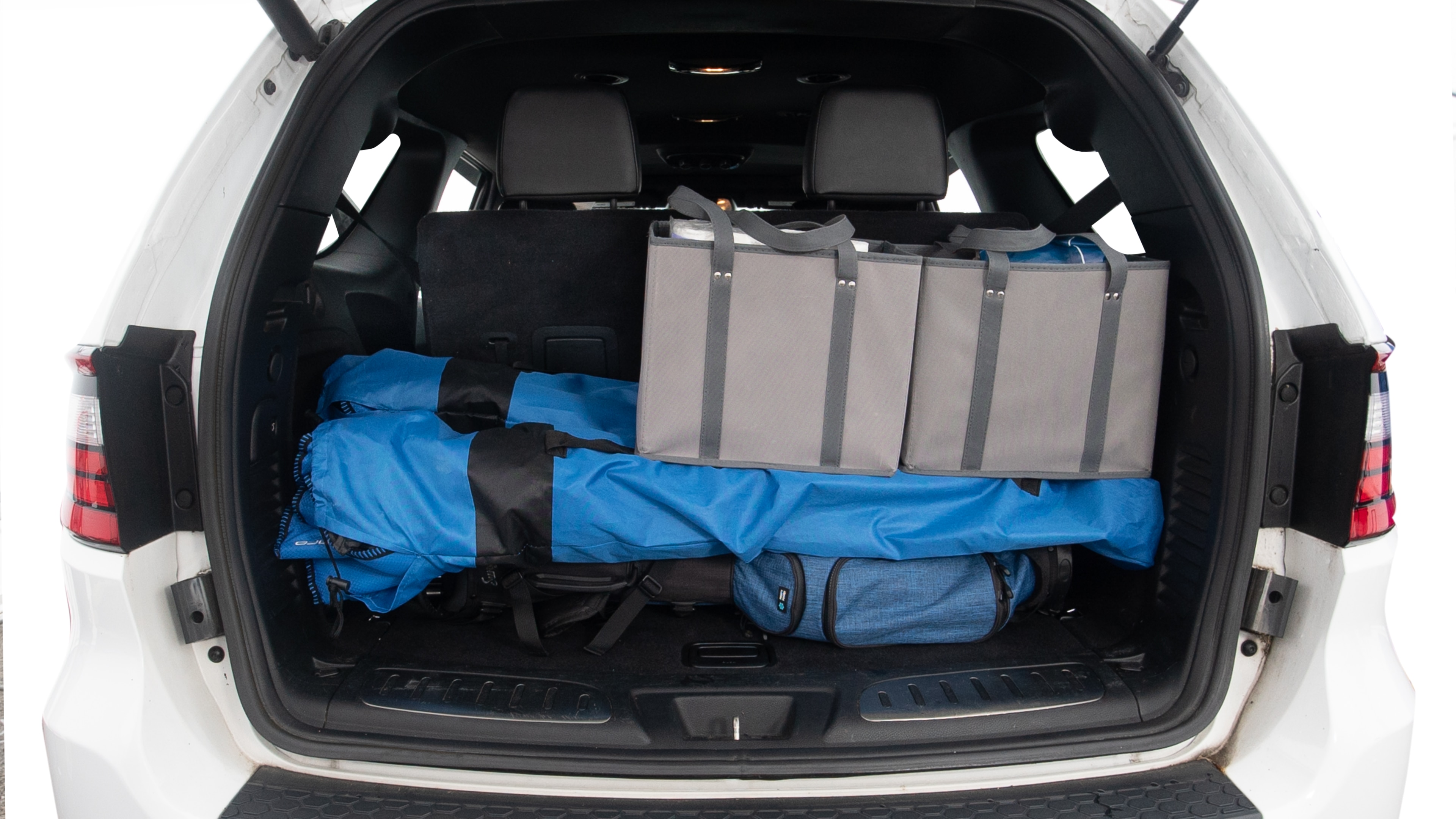 The trunk lid is open showing full view of the trunk. Three grocery carriers, two camping chairs in the carrying bag, and a set of golf clubs are placed inside.