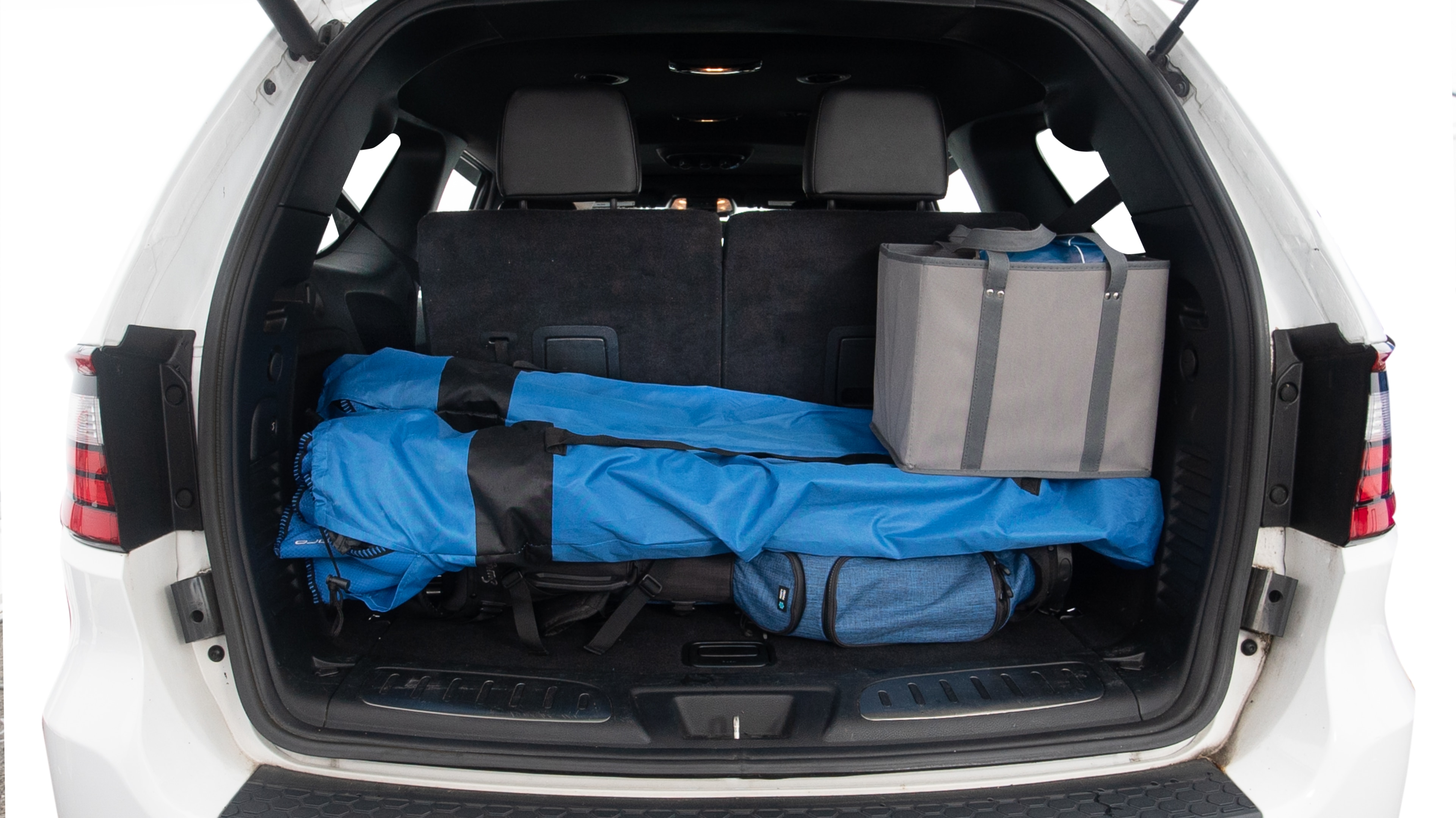 The trunk lid is open showing full view of the trunk. Three grocery carriers, two camping chairs in the carrying bag, and a set of golf clubs are placed inside.