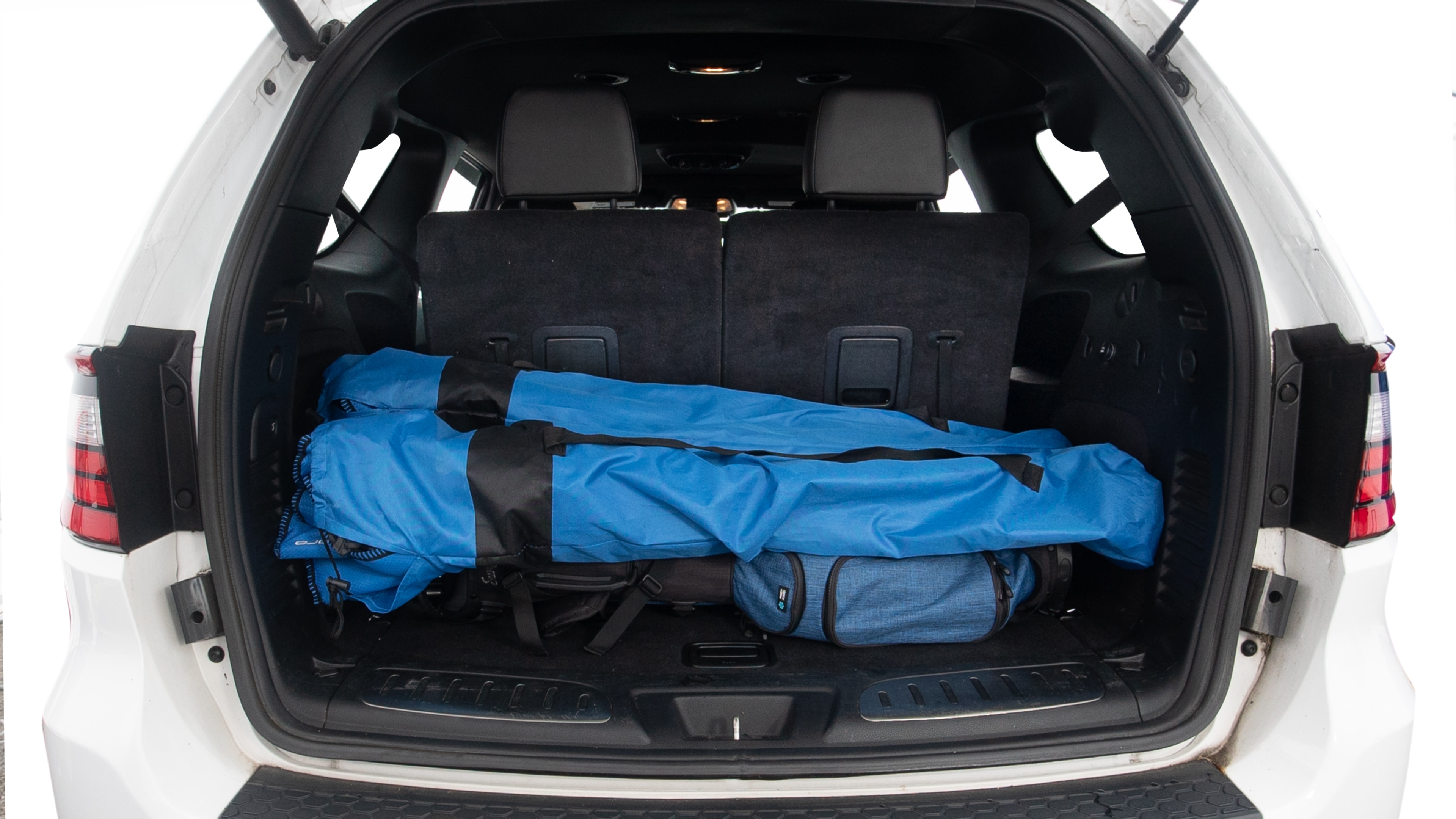 The trunk lid is open showing full view of the trunk. Three grocery carriers, two camping chairs in the carrying bag, and a set of golf clubs are placed inside.